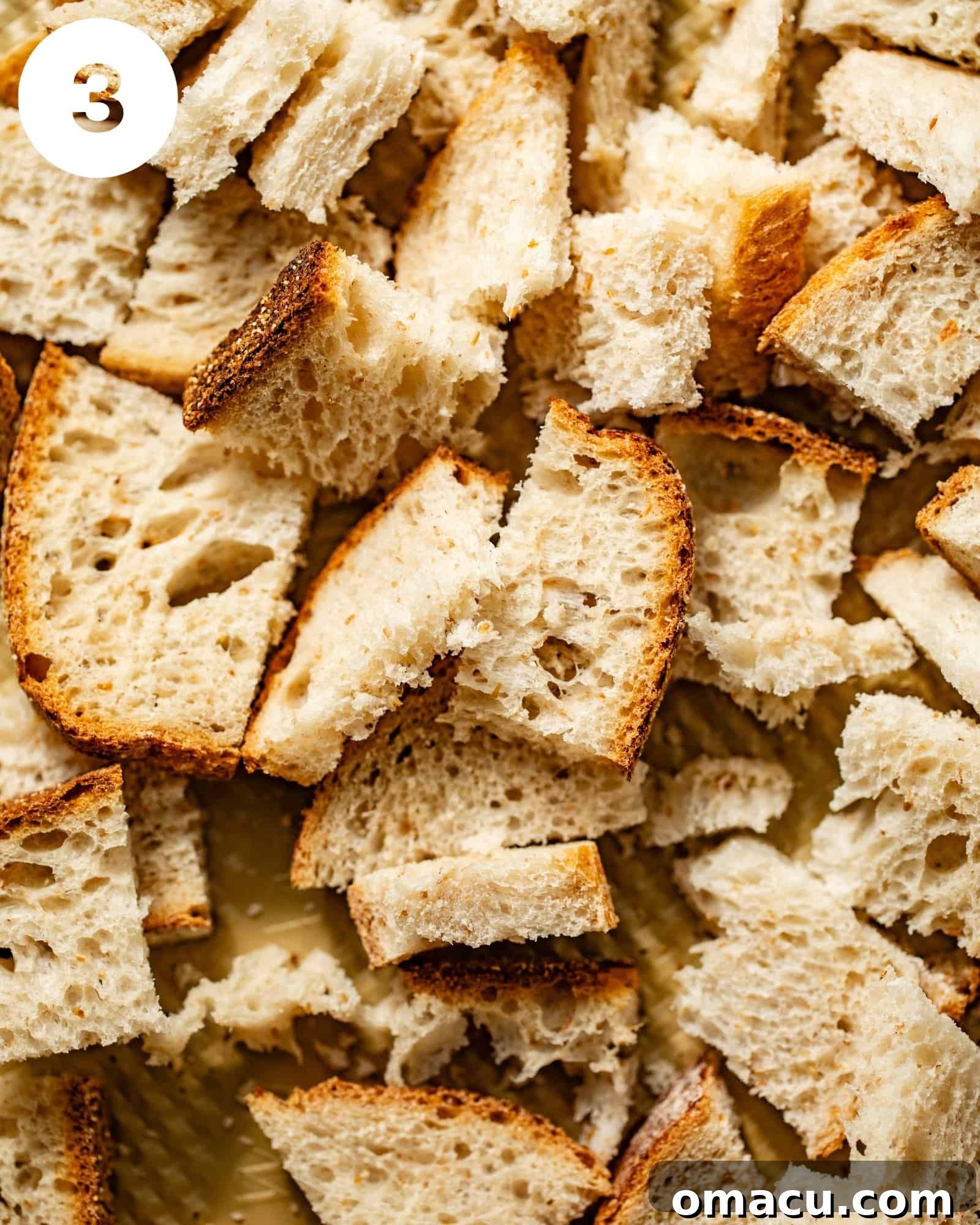 Sourdough bread cut into uniform chunks and spread on a baking sheet, ready for the oven to become crispy croutons.