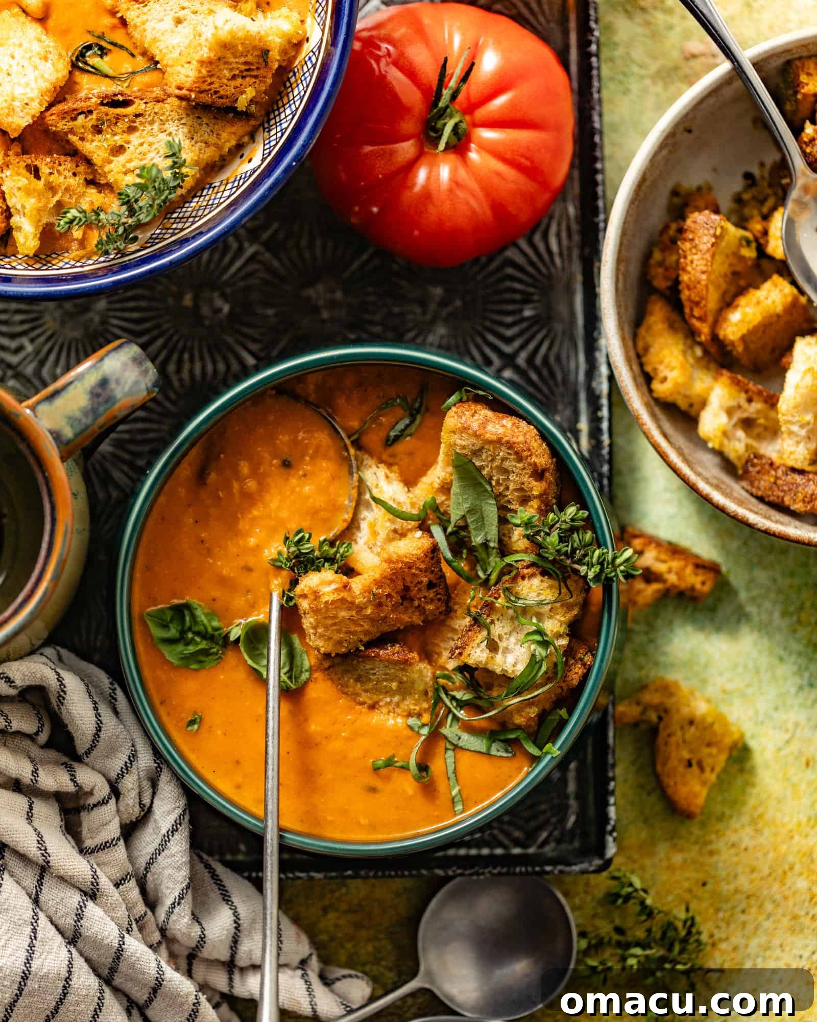 An overhead photo of multiple bowls of heirloom tomato soup, beautifully garnished with homemade garlic croutons and fresh herbs, ready to be served.
