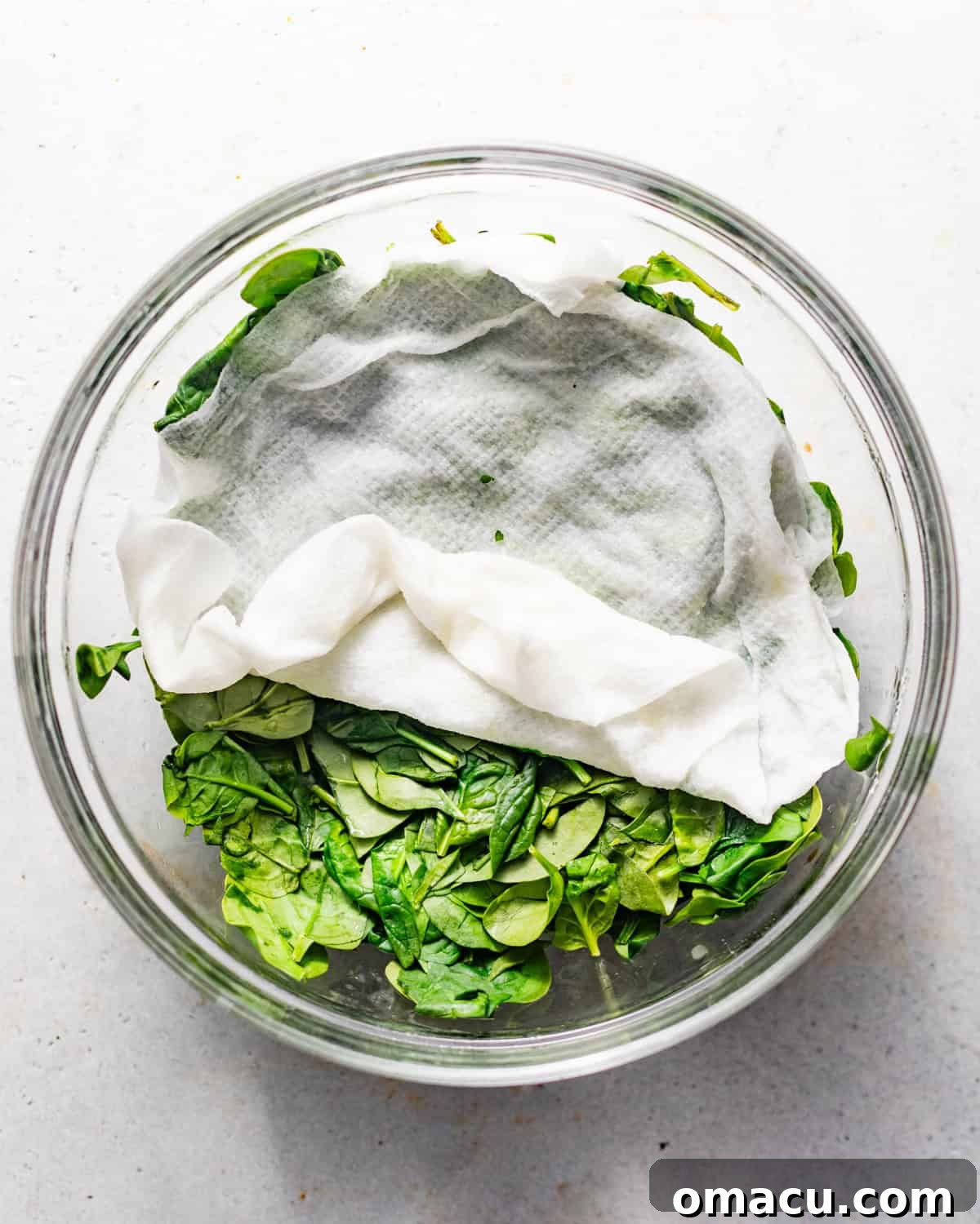 Fresh baby spinach in a large bowl, covered with a damp paper towel, ready for wilting.