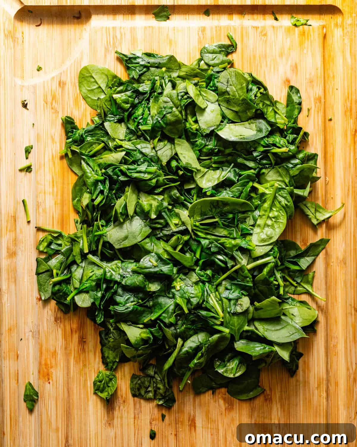 Roughly chopped and squeezed spinach on a cutting board, showing removed moisture.