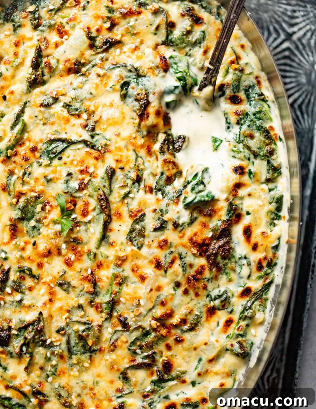 Broiled creamed spinach in an oven-safe serving tray, garnished with golden-brown cheese and a serving spoon.