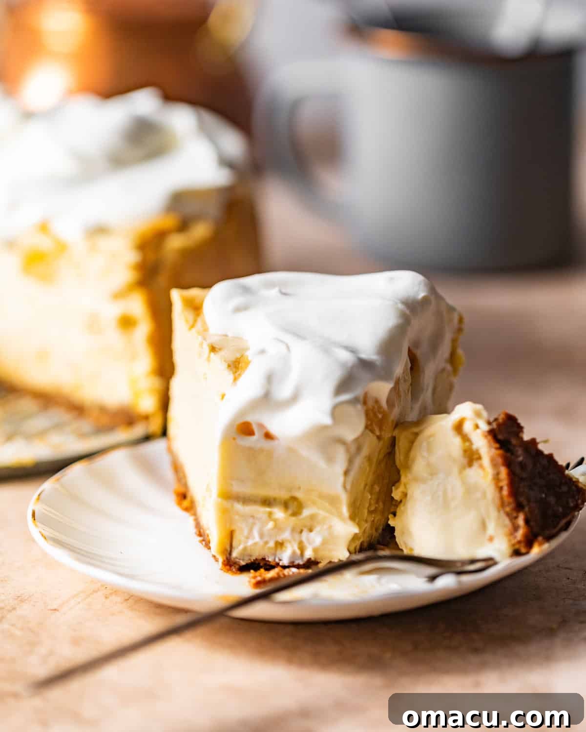 A perfectly sliced piece of creamy pineapple cheesecake on a white plate, garnished with fresh pineapple, with a fork beside it.