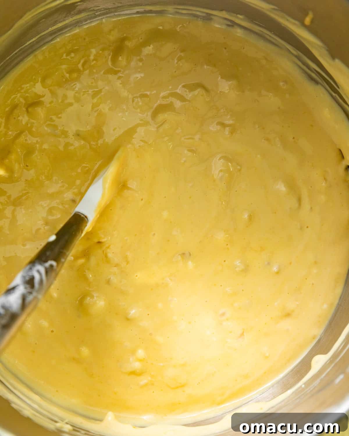 The pineapple mixture being gently folded into the cream cheese batter in a stand mixer bowl using a paddle attachment.