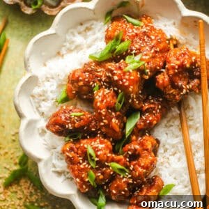 Crispy orange chicken and rice served in a bowl with chopsticks.