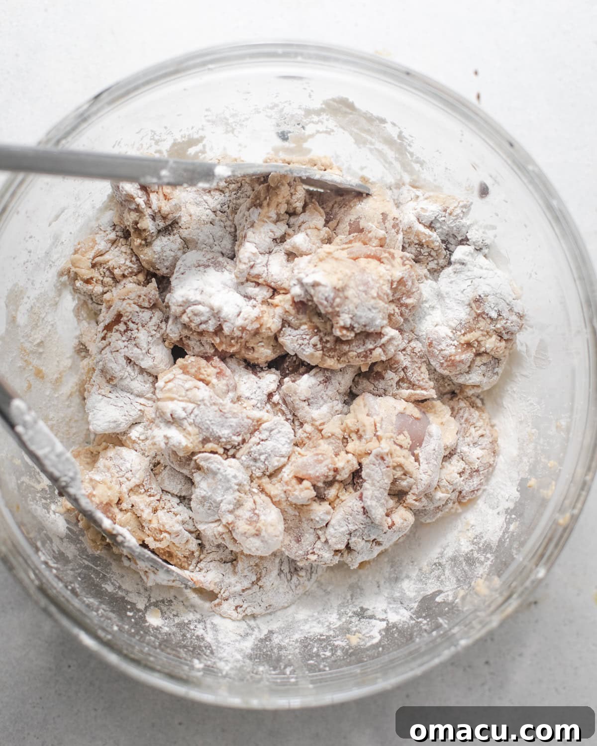 Chicken thighs cut into pieces and covered in a thick flour coating in a bowl, ready for frying.