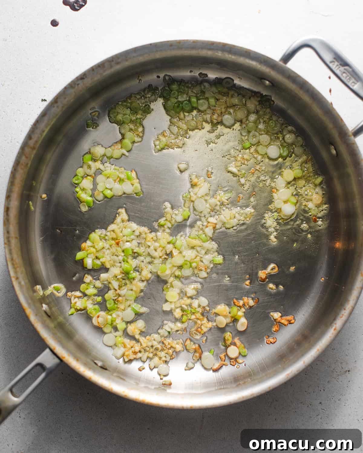Sautéed garlic and ginger sizzling in a skillet with sesame oil, forming the aromatic base of the sauce.
