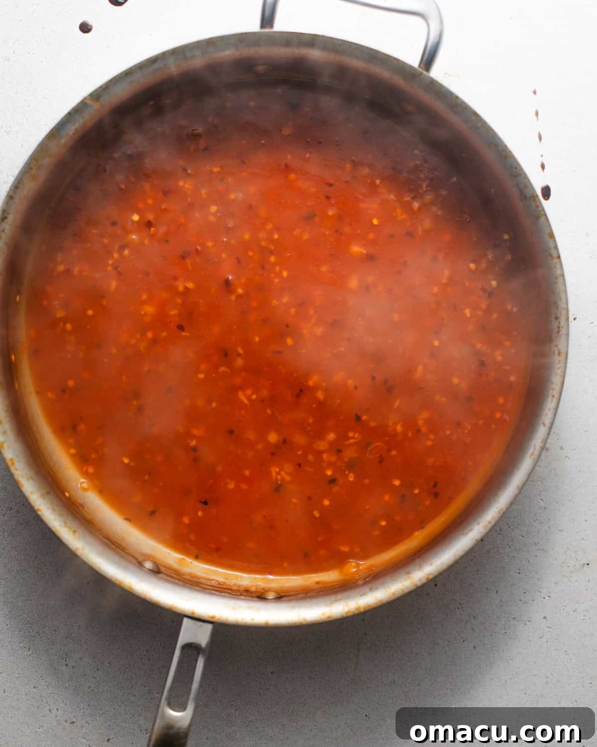 Orange chicken sauce simmering in a skillet, thickening to a glossy consistency.