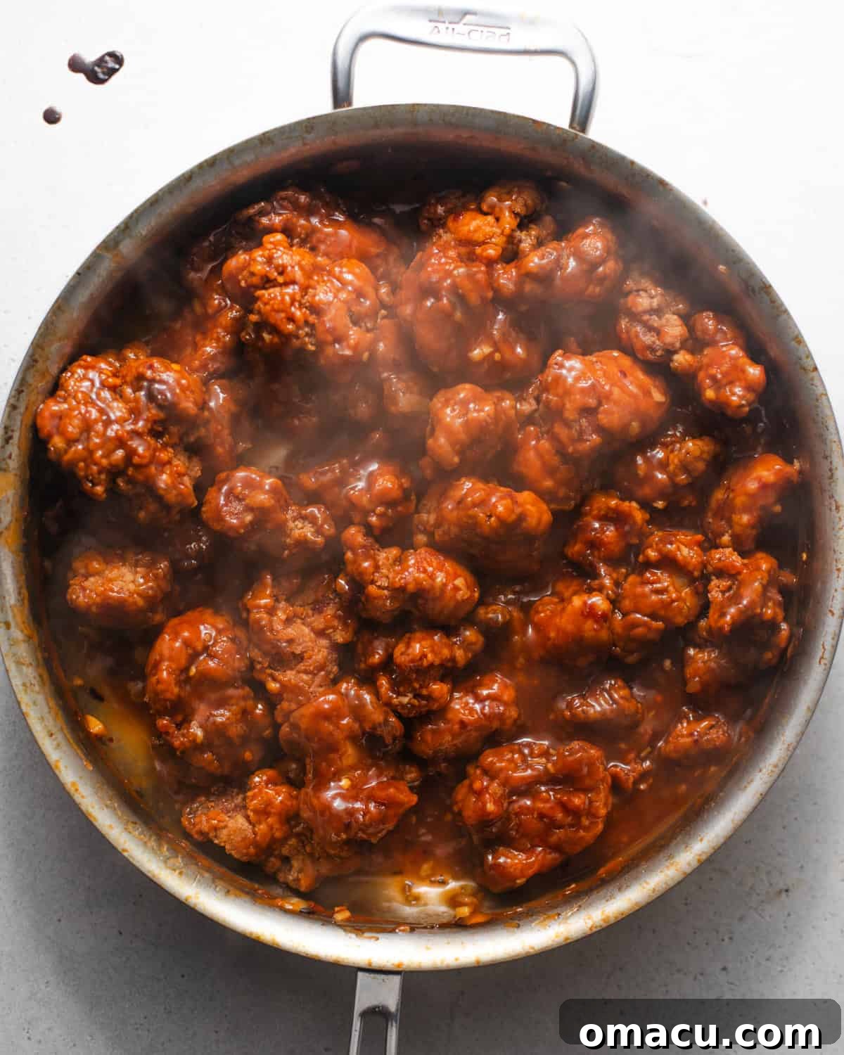 Crispy orange chicken pieces being tossed in the glossy orange sauce in a skillet.