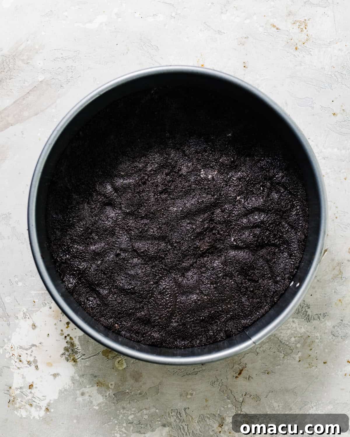 A dark, uniform Oreo cookie crust tightly pressed into the bottom of a silver springform pan, ready for the filling.