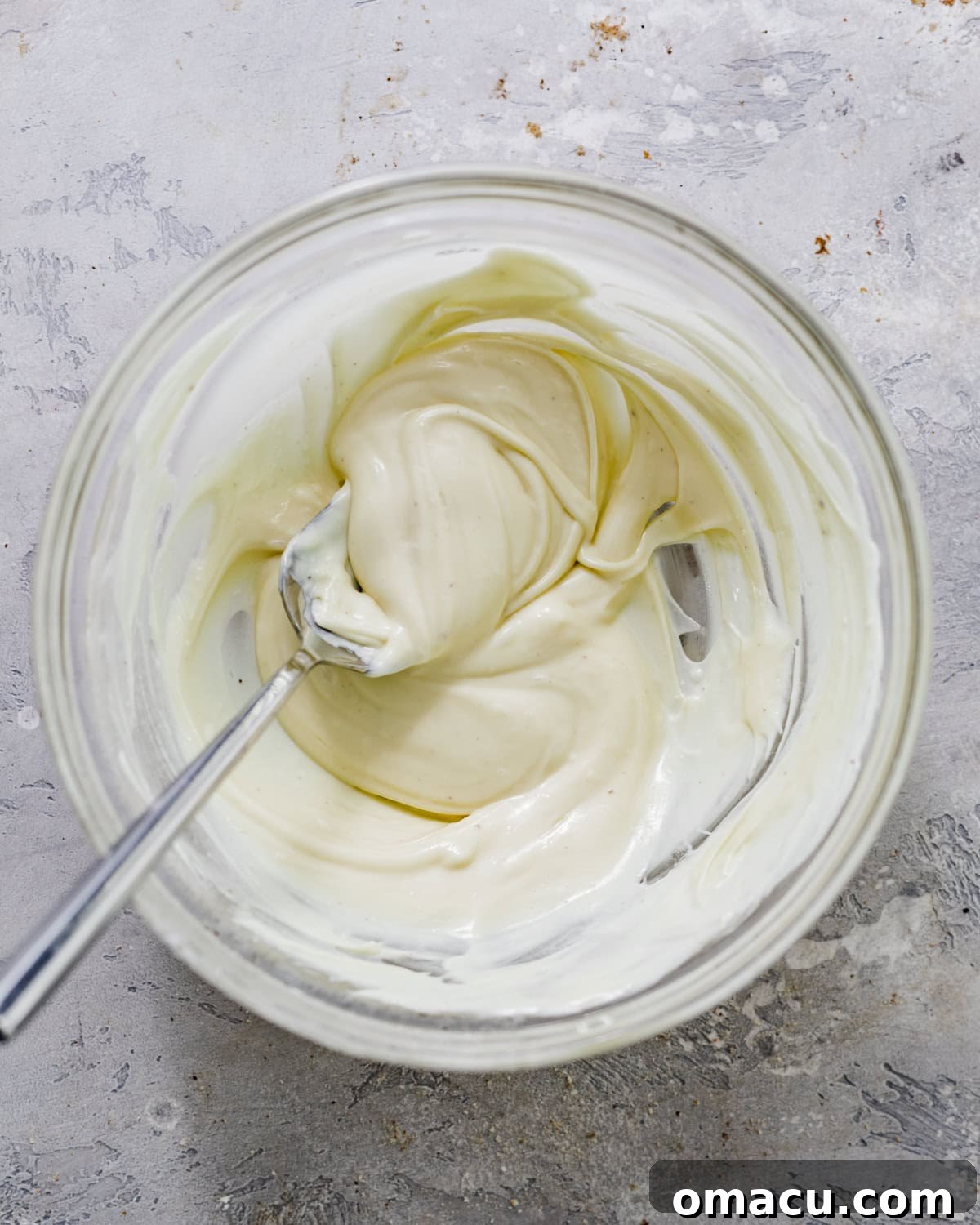 A small glass bowl containing smooth, glossy melted white chocolate, ready to be incorporated into the cheesecake filling.
