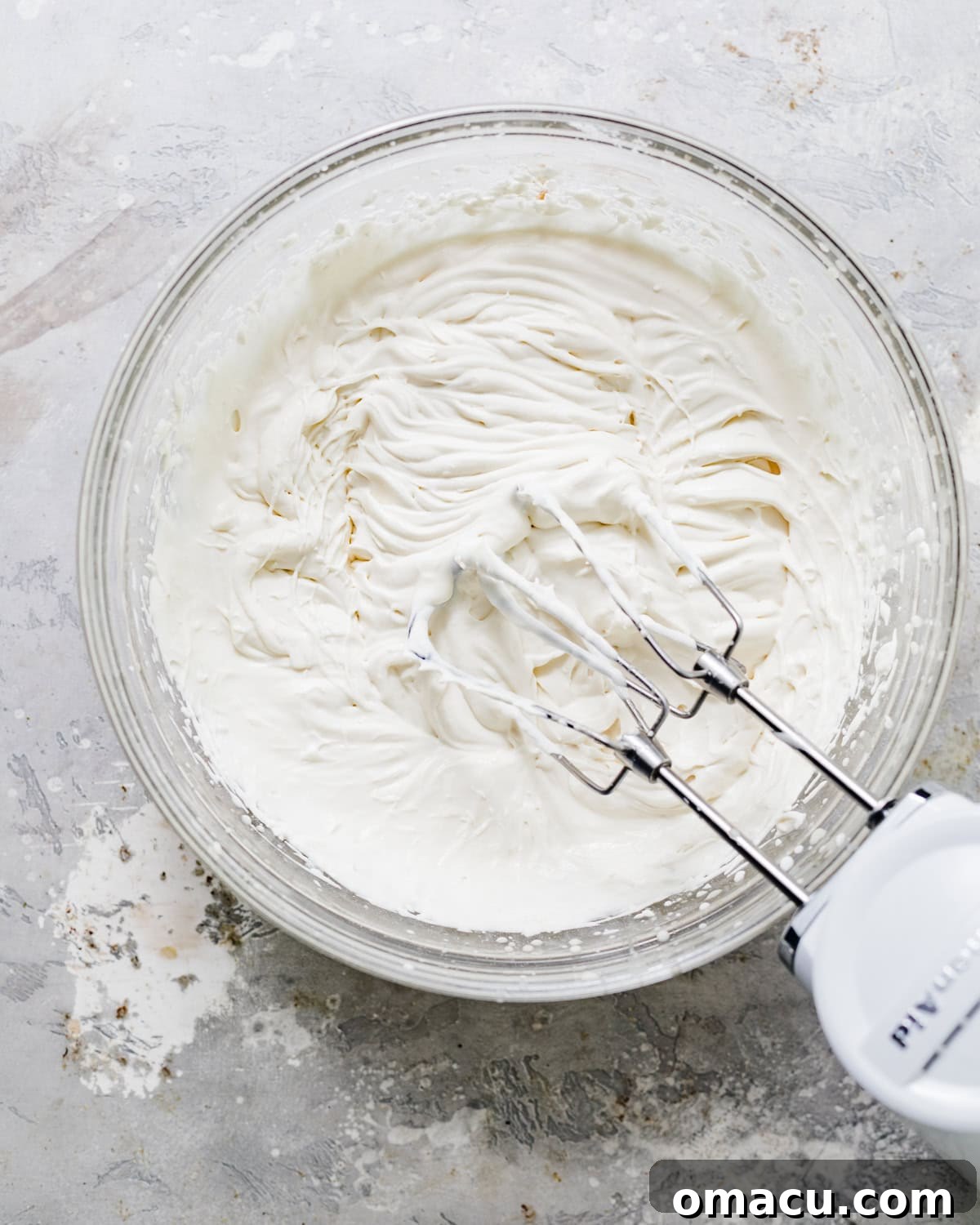 A separate mixing bowl filled with heavy cream, perfectly whipped to stiff peaks, ready to be incorporated into the cheesecake mixture.