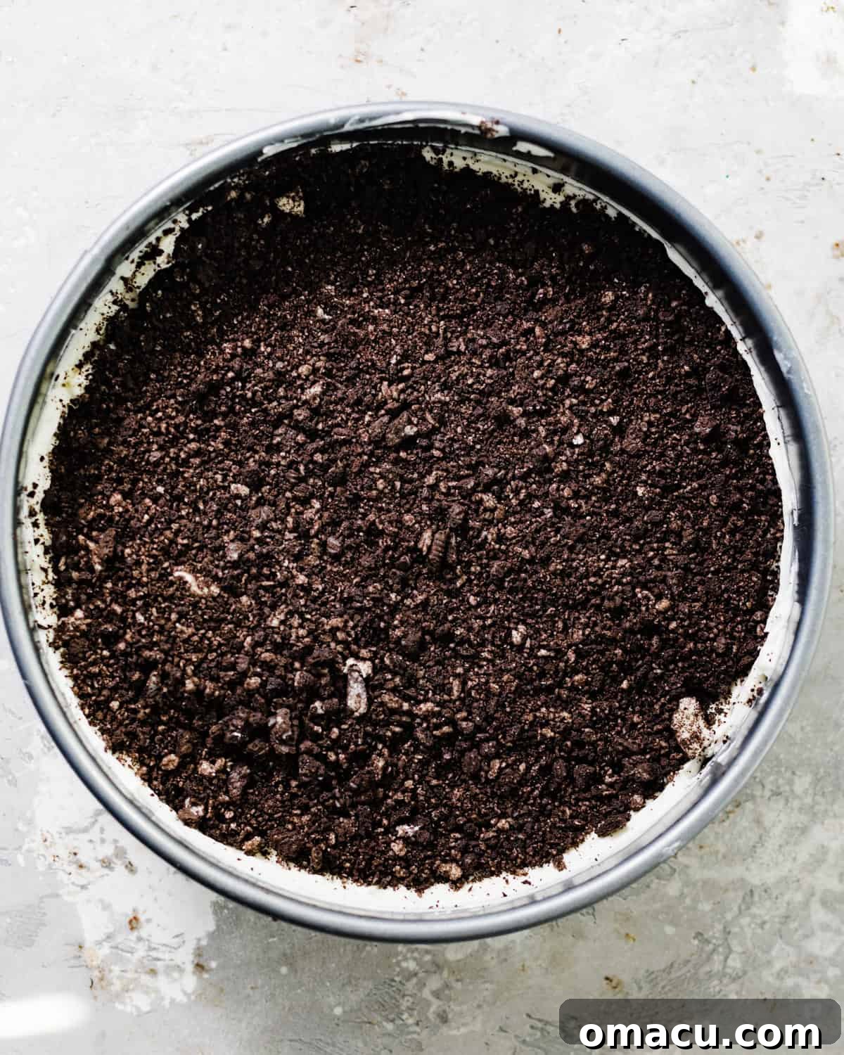Half of the creamy cheesecake batter spread over the Oreo crust in a springform pan, with a generous layer of crushed Oreos sprinkled on top.