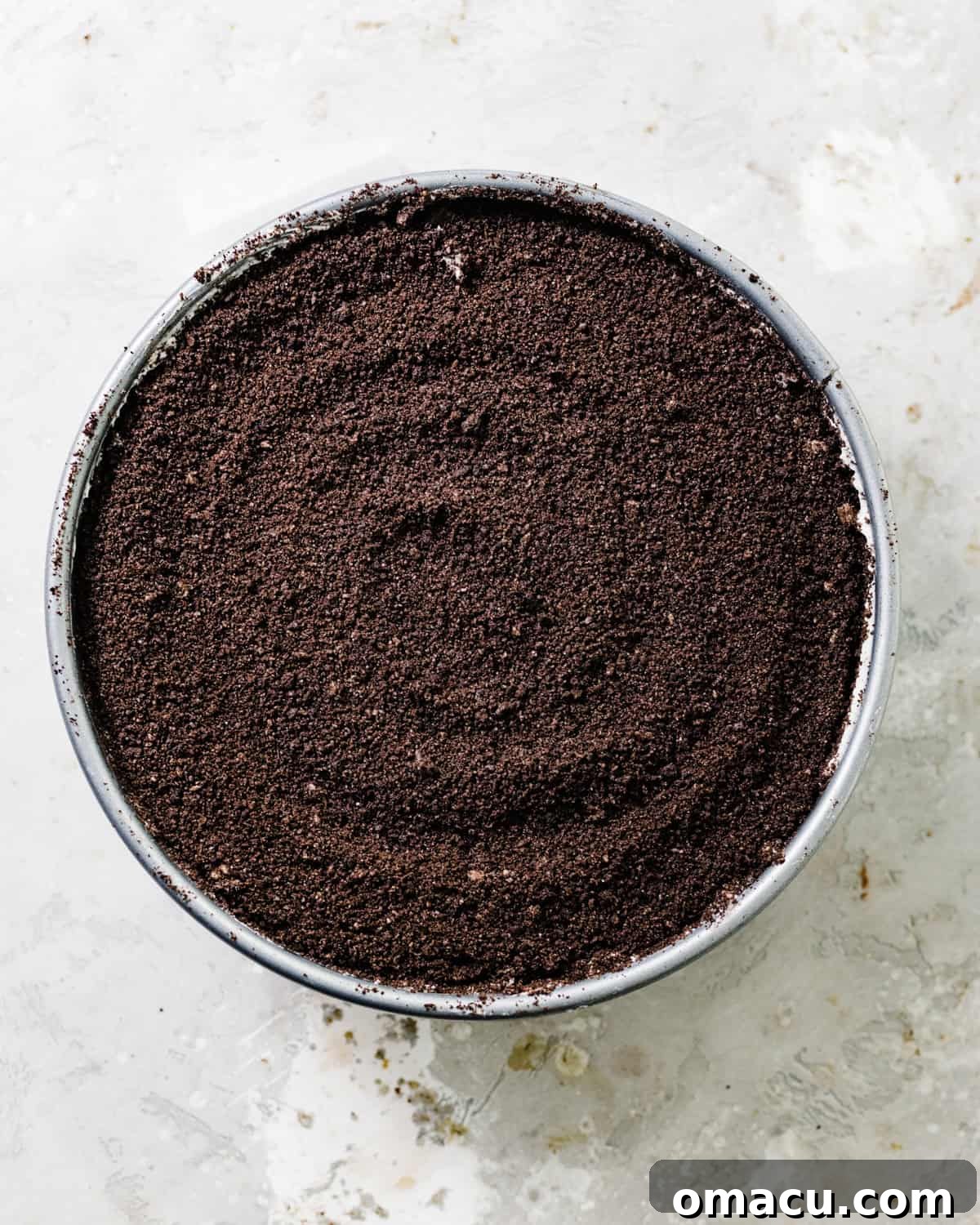 A completed no-bake Oreo cheesecake in a springform pan, generously topped with crushed Oreos, ready for chilling.