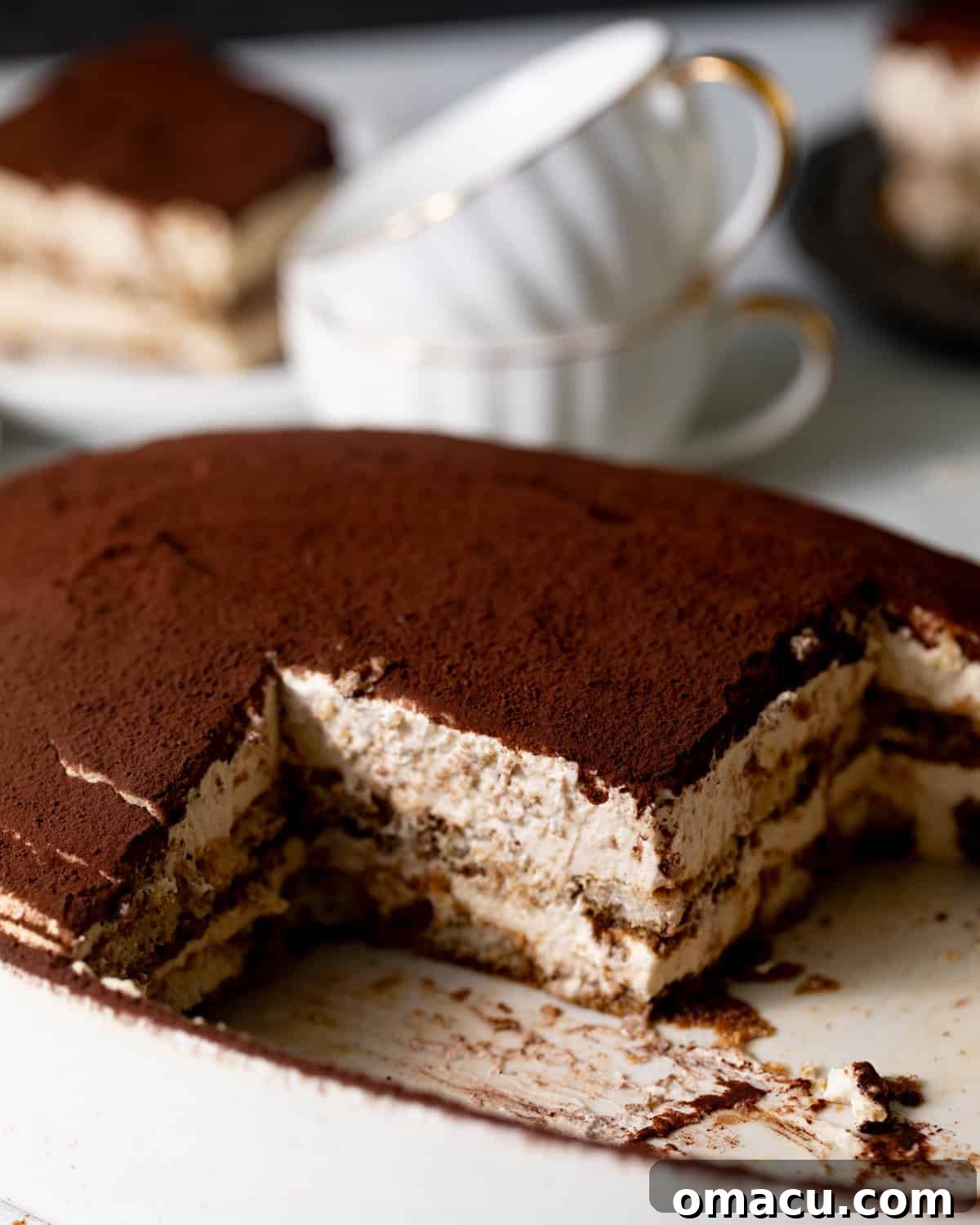 A perfectly layered authentic Italian Tiramisu in an elegant oval dish, with a slice removed to reveal its luscious, layered center of coffee-soaked ladyfingers and creamy mascarpone.