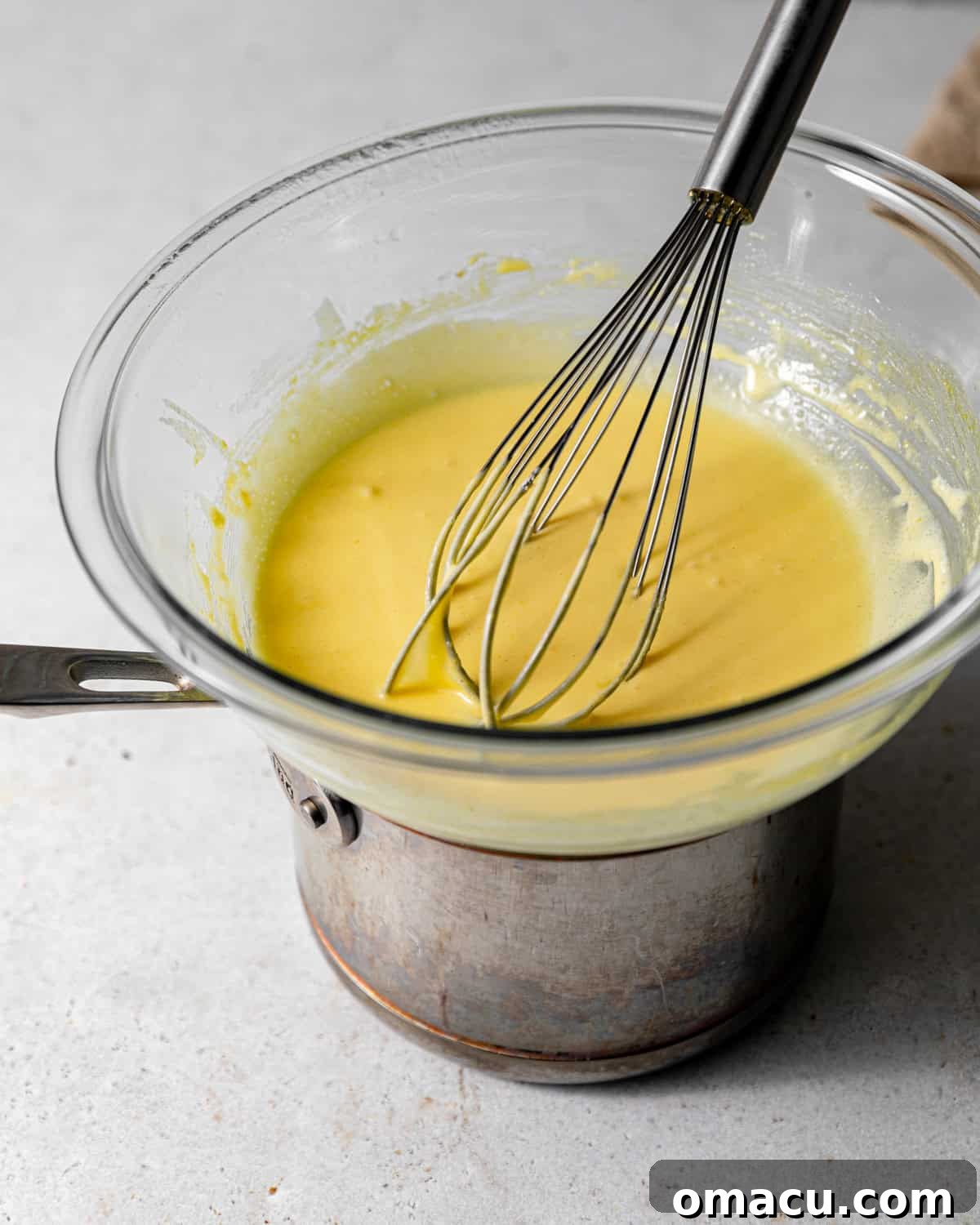 Egg yolks and granulated sugar being whisked together in a heat-safe bowl set over a double boiler, demonstrating the first step in creating the creamy mascarpone base for tiramisu.