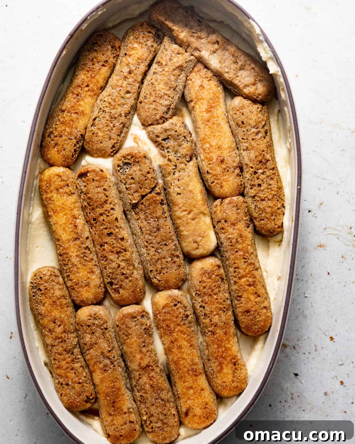 Dipped ladyfingers neatly lined up in a 9x13 inch baking dish, forming the first layer of an authentic Italian tiramisu.