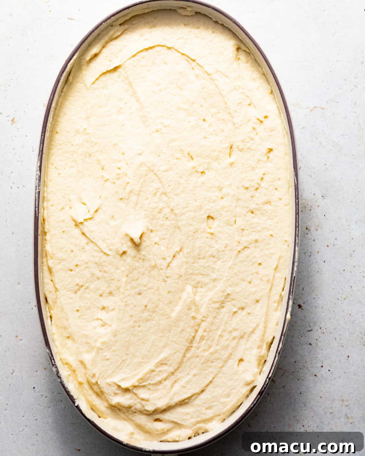 A fully assembled tiramisu in a baking dish, with the final layer of creamy mascarpone spread smoothly, ready for chilling and dusting with cocoa powder.