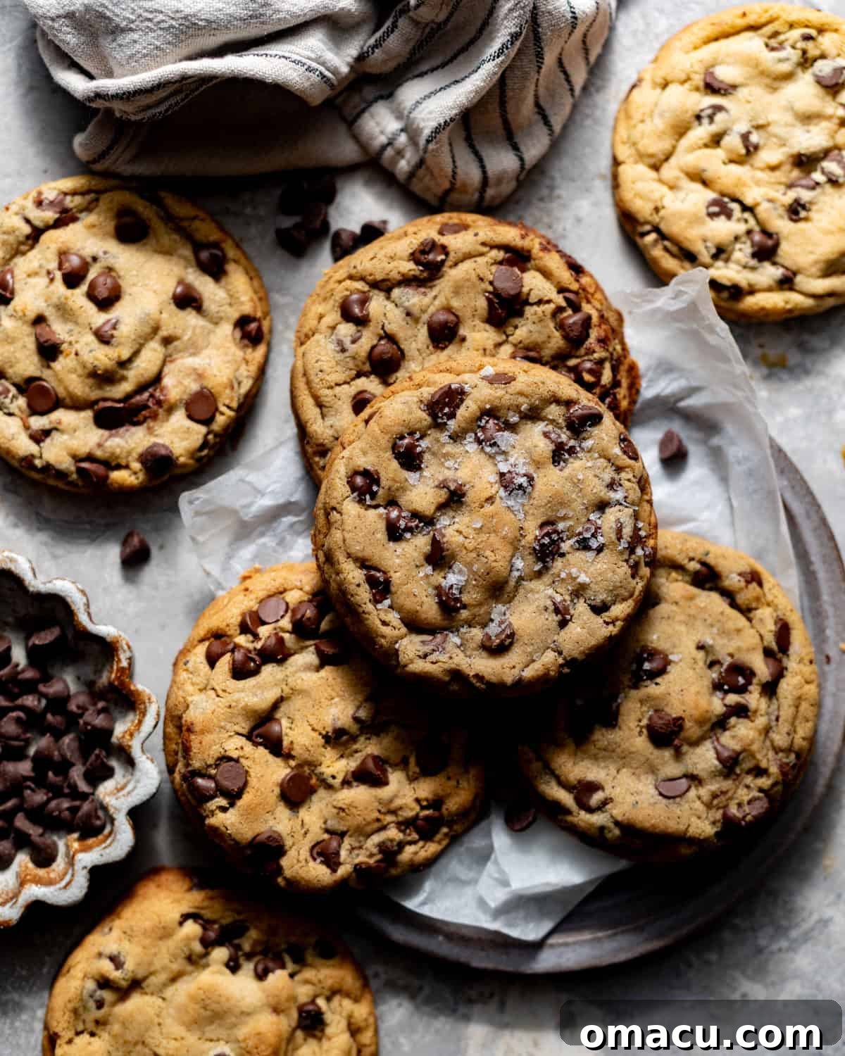 Perfectly baked brown butter chocolate chip cookies, stacked on a plate with parchment paper and sprinkled with flaky salt, invitingly warm.