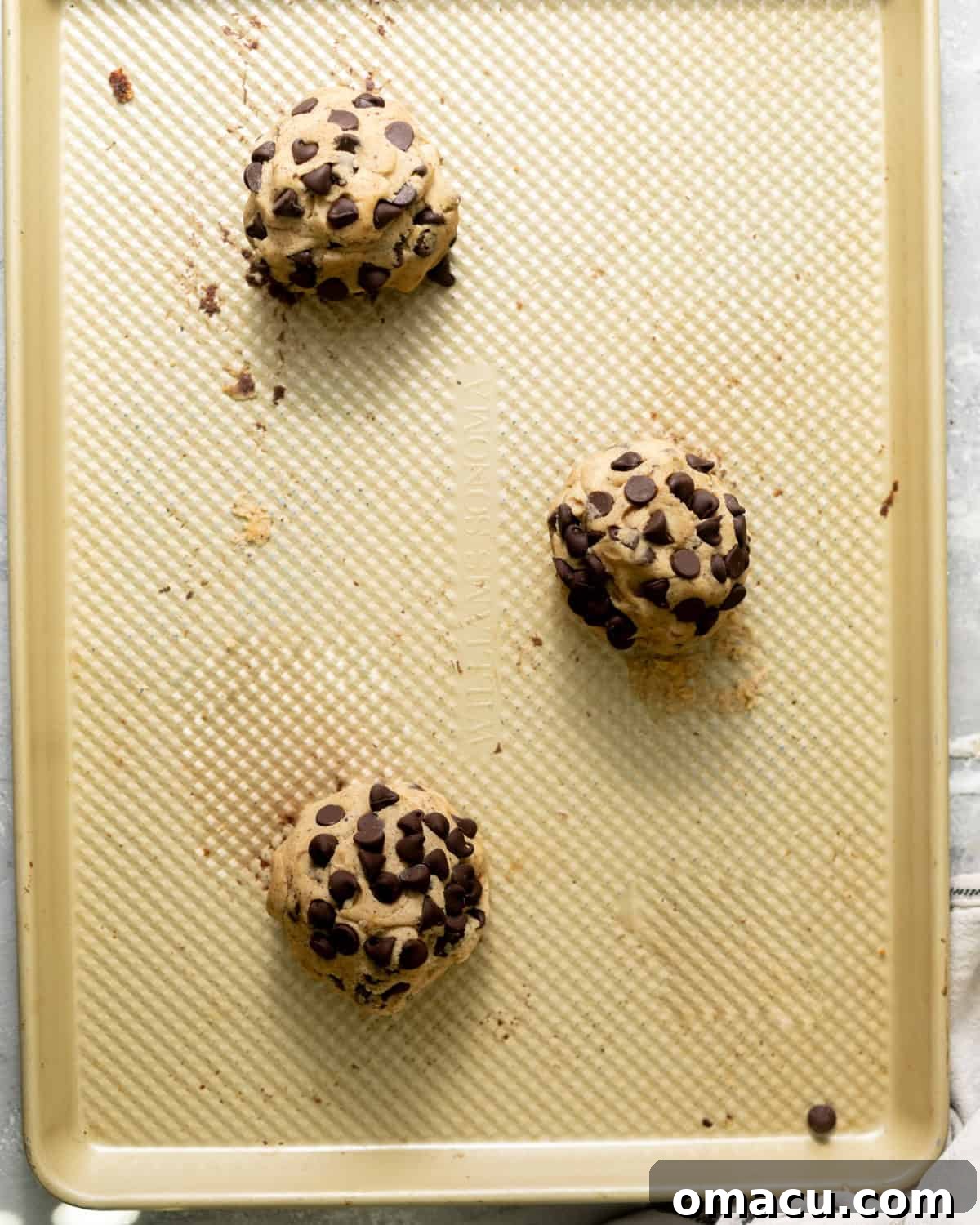 Three perfectly spaced cookie dough balls on a baking sheet, ready for baking in a preheated oven.