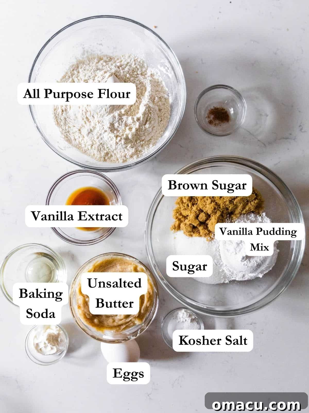 A curated display of essential ingredients for making chocolate chipless cookies, including flour, butter, salt, baking soda, both brown and white sugar, vanilla extract, vanilla pudding mix, and eggs.