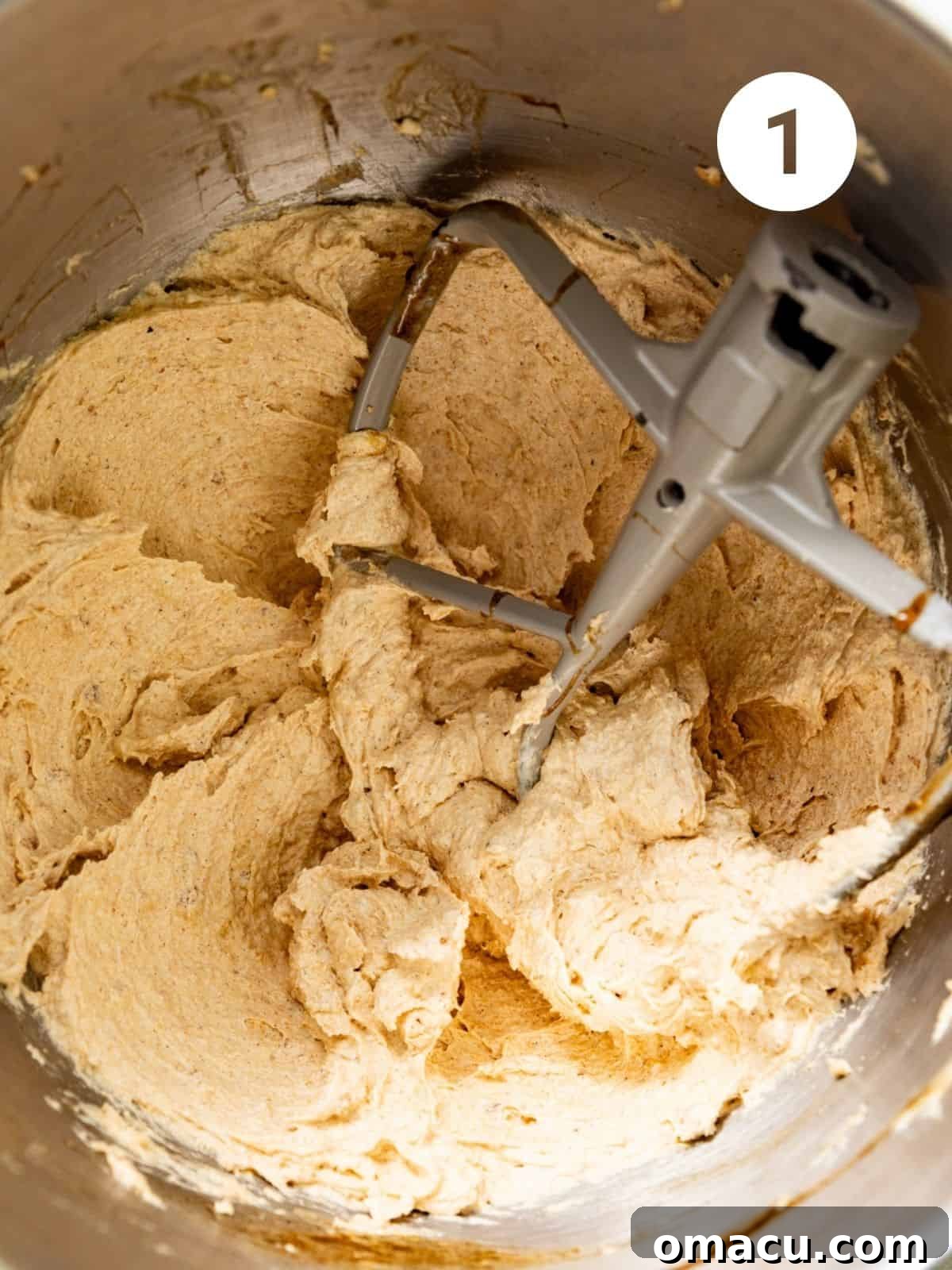 A mixing bowl containing a creamy, light yellow mixture of butter, sugars, eggs, vanilla extract, and vanilla pudding mix, ready for the dry ingredients.