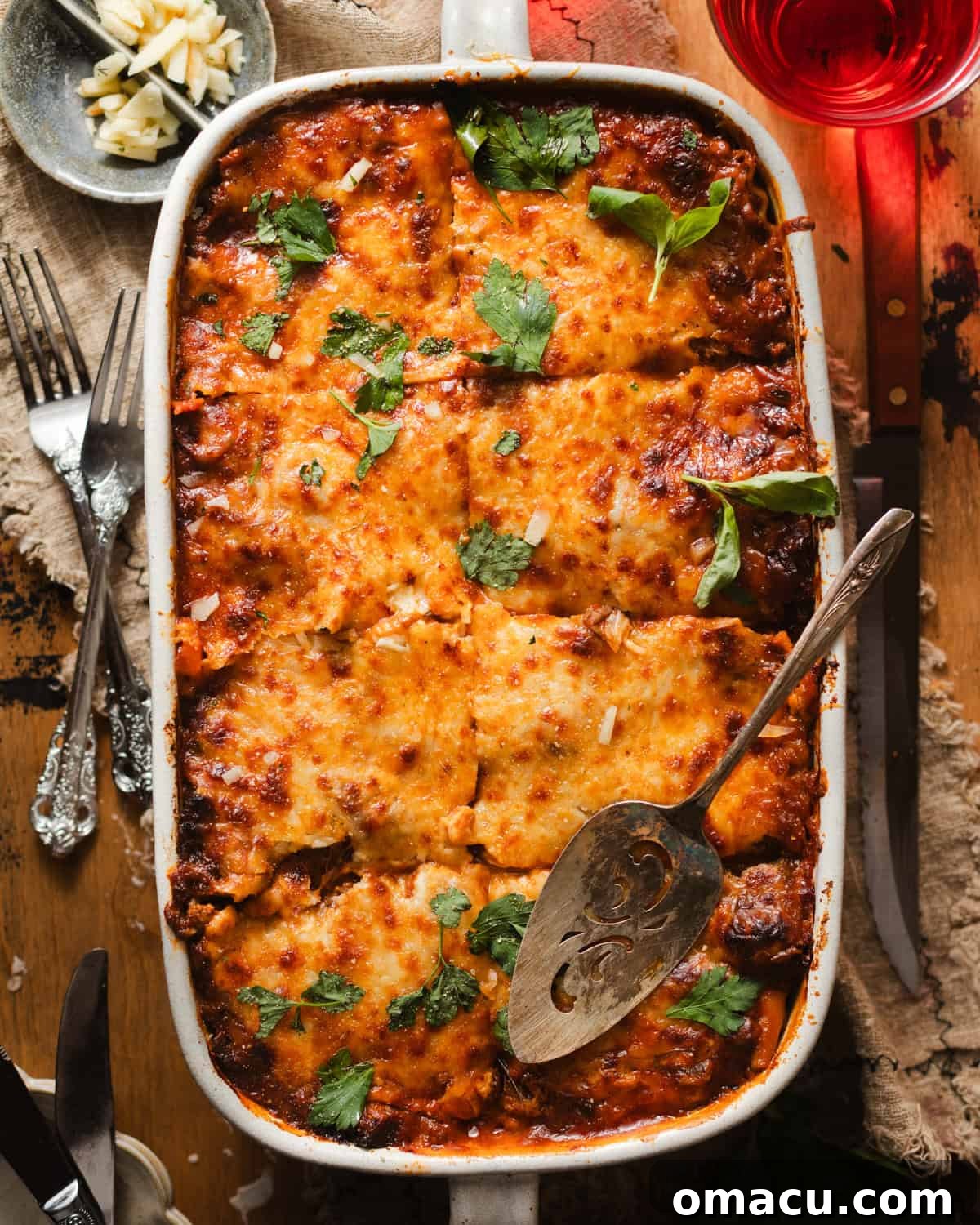 lasagna alla bolognese in a lasagna pan with a serving spoon and fresh chopped parsley and basil.