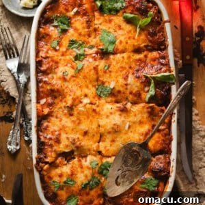 lasagna alla bolognese in a lasagna pan with a serving spoon and fresh chopped parsley and basil.