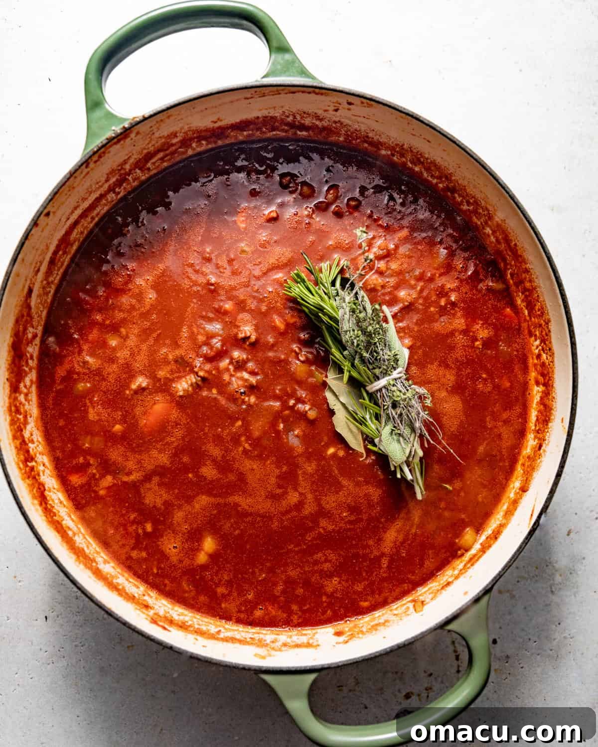 bolognese sauce assembled in a pot with fresh herbs tied in a bunch and parmesan rind on top. 