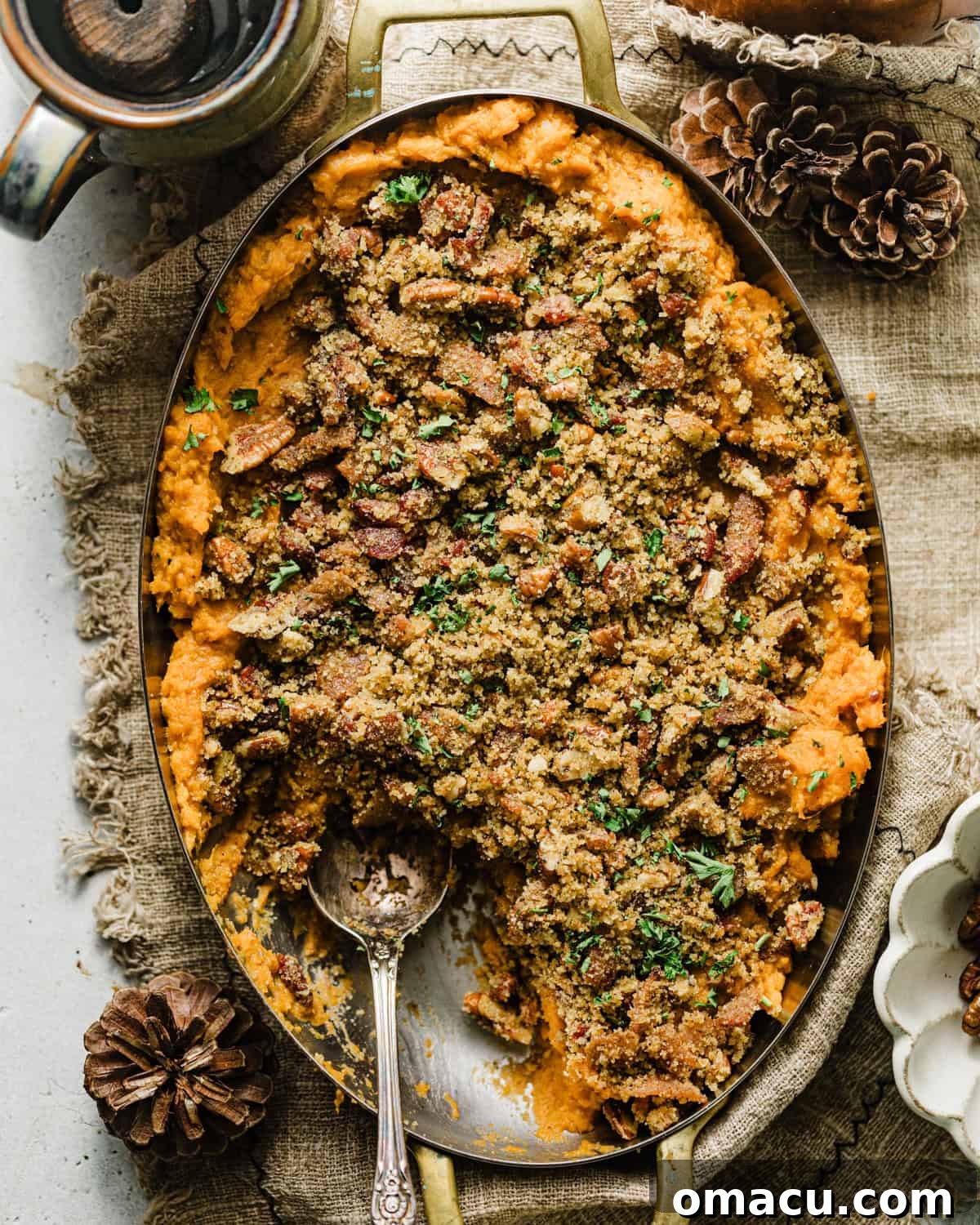 Savory sweet potato casserole in an oval casserole dish topped with a bacon and pecan breadcrumb topping, ready to be served.