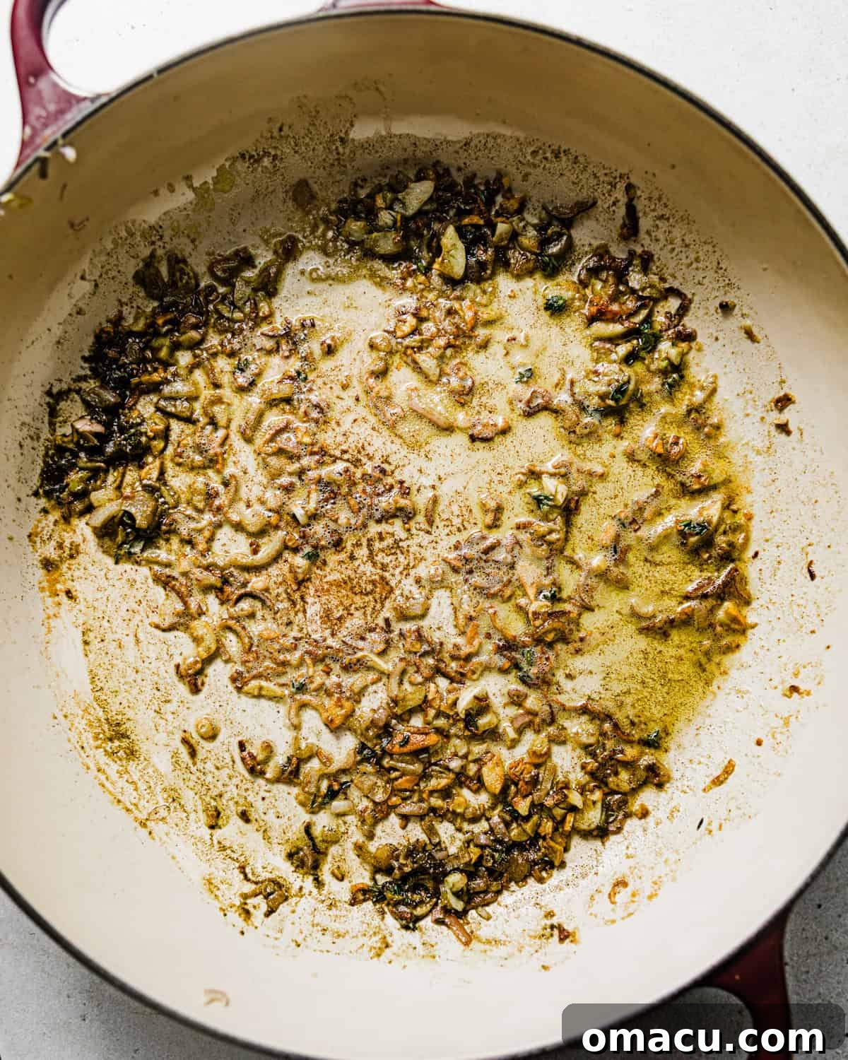 Shallots, fresh herbs, and seasonings sautéed in a skillet, creating an aromatic mixture.