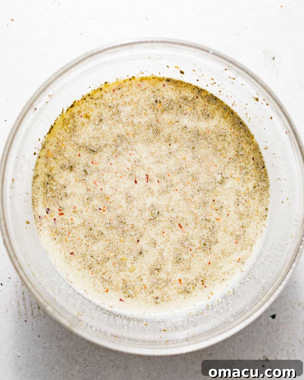 Milk, heavy cream, eggs, and seasonings being vigorously whisked in a large mixing bowl to form the custard.