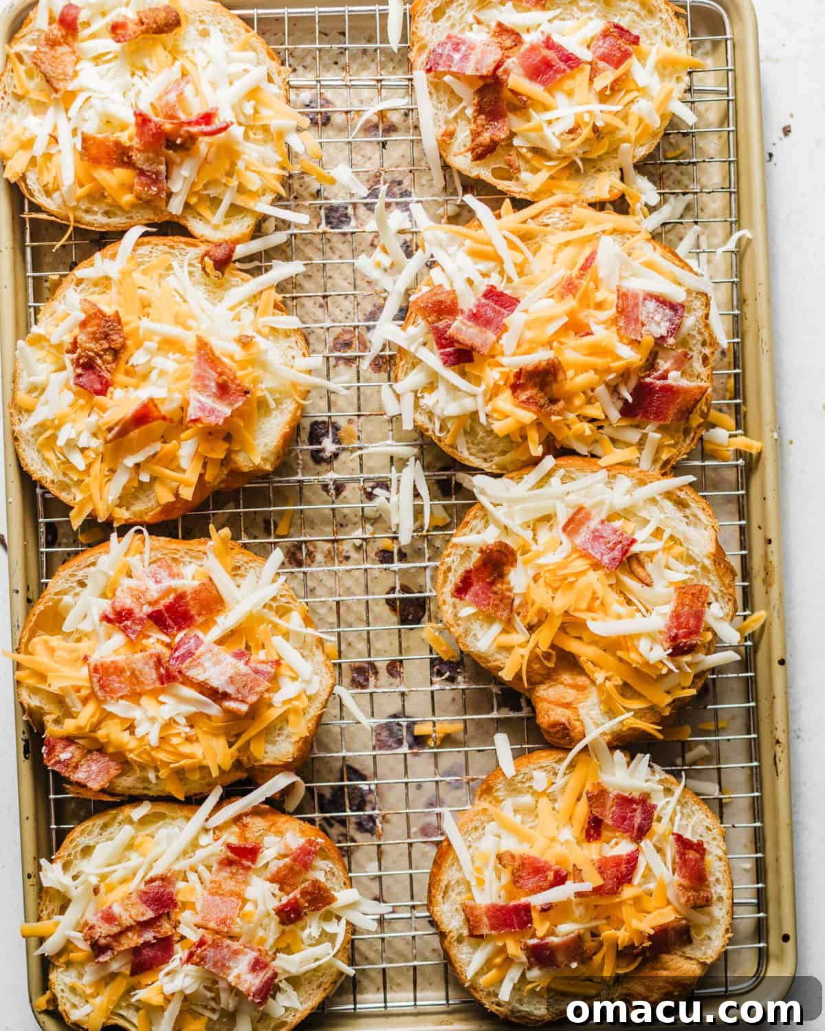 Halved croissants being topped with shredded cheese and crispy bacon pieces before being reassembled.