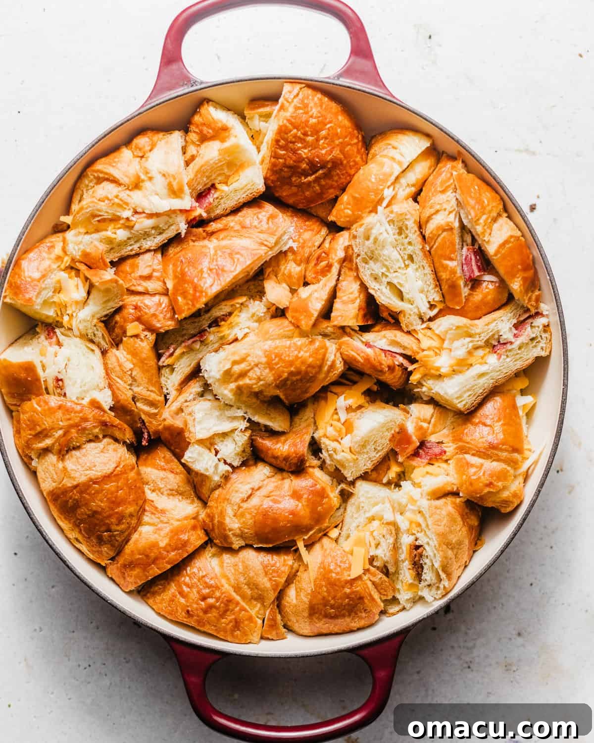 Bite-sized croissant pieces filled with bacon and cheese, neatly arranged in a round casserole dish.