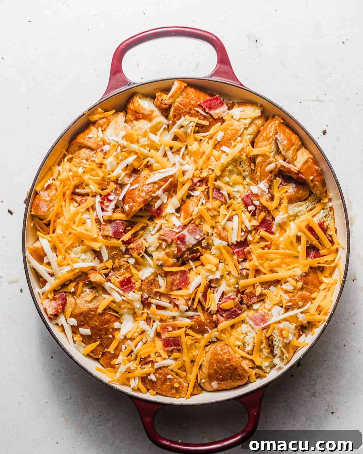 The assembled croissant breakfast casserole, ready for baking, topped with a final layer of shredded cheese.