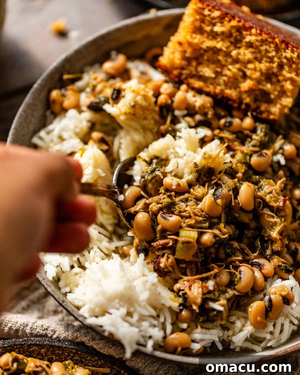 A close-up shot of a bowl of black-eyed peas and collard greens, served with rice and a hand spooning more of the delicious food, emphasizing its comforting appeal.