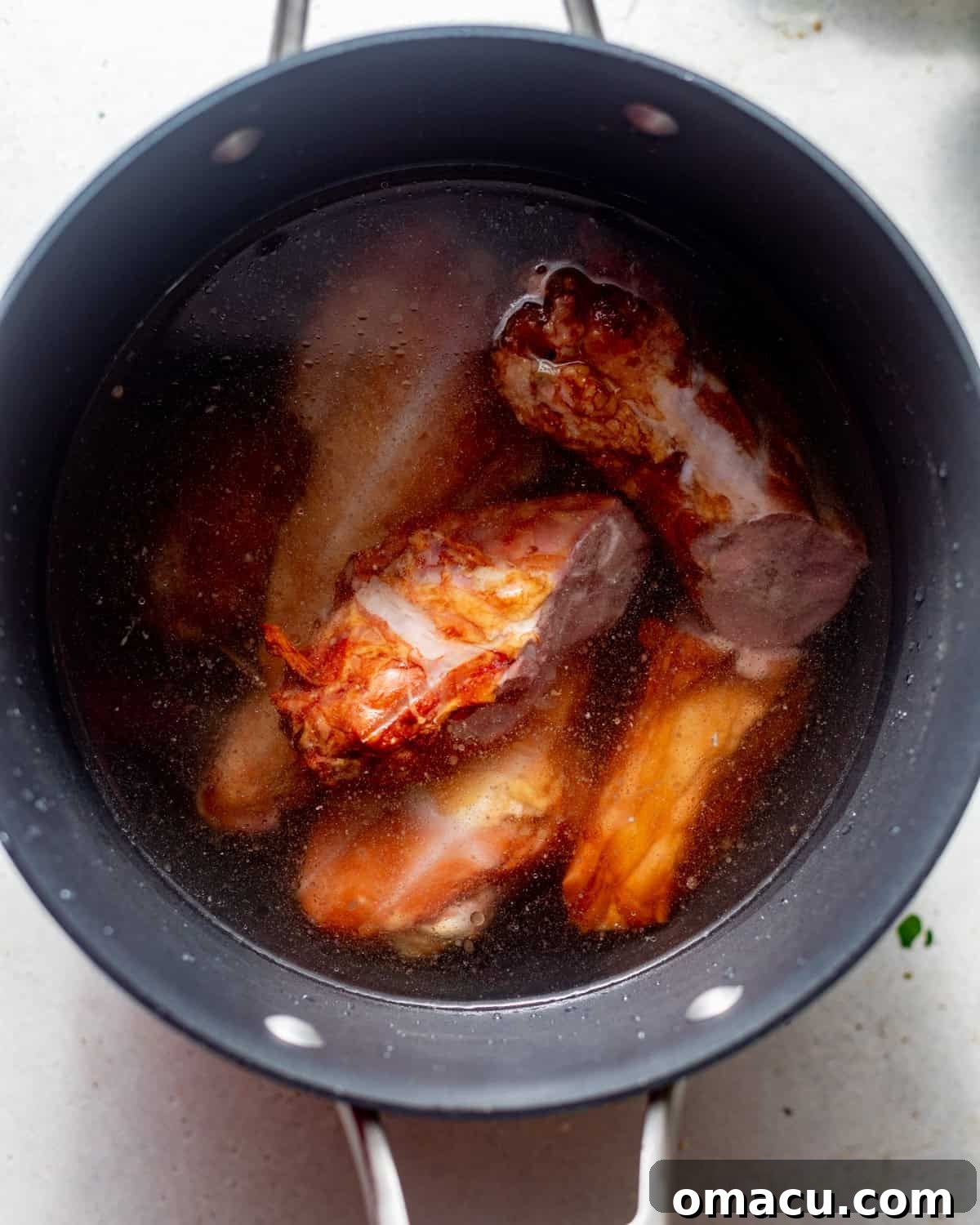 Smoked turkey neck and legs simmering in a large stockpot with water, fresh thyme, bay leaves, and chicken bouillon paste, creating a rich broth.