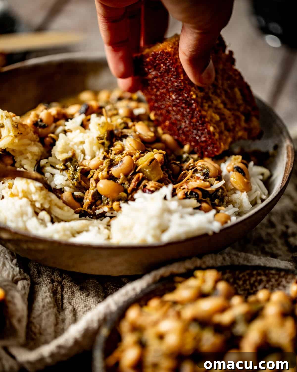 A bowl of black-eyed peas with collard greens, with a hand dipping a piece of cornbread into the flavorful potlikker, illustrating a classic Southern eating experience.