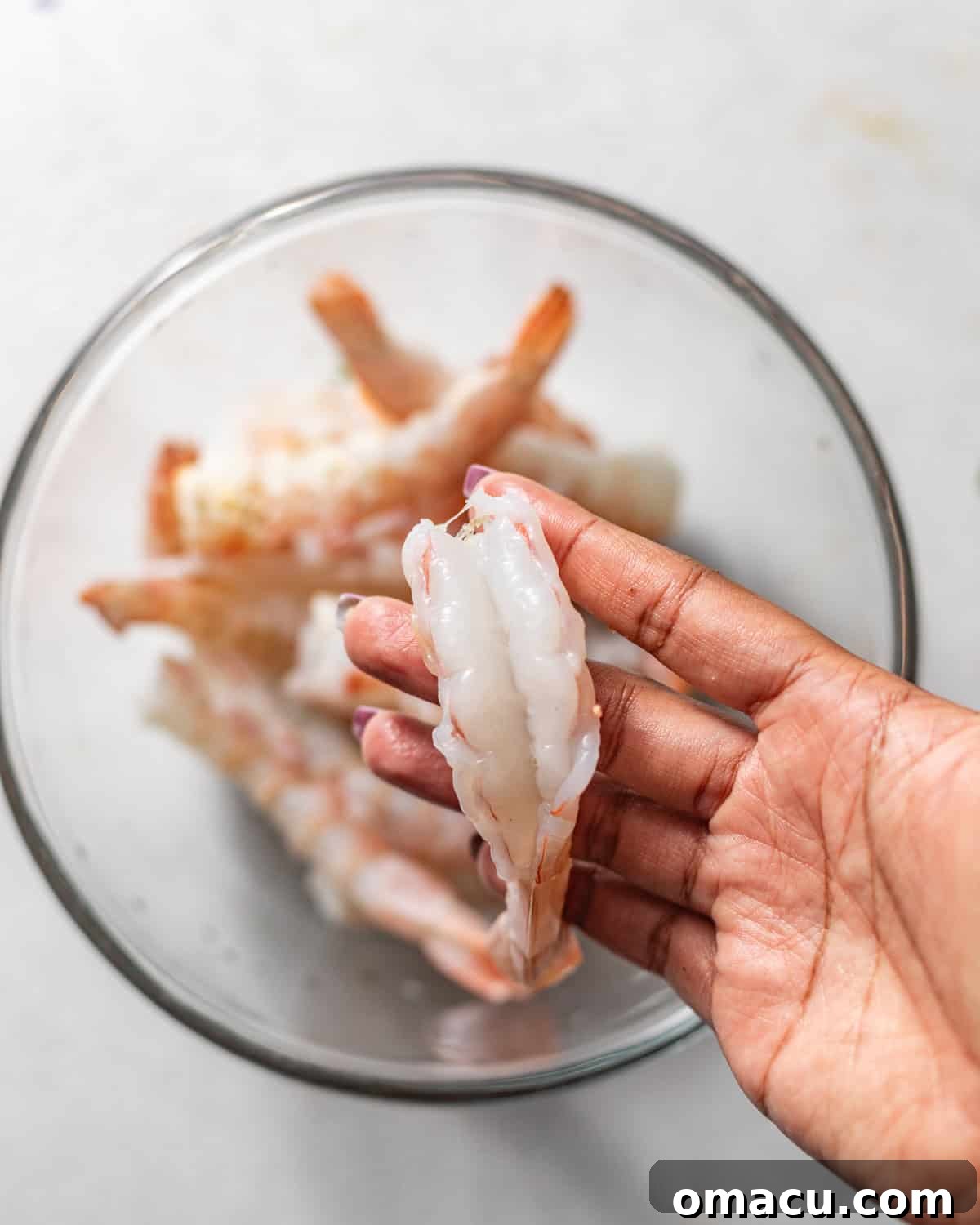 A close-up of a hand skillfully holding a perfectly butterflied shrimp, demonstrating the preparation technique.