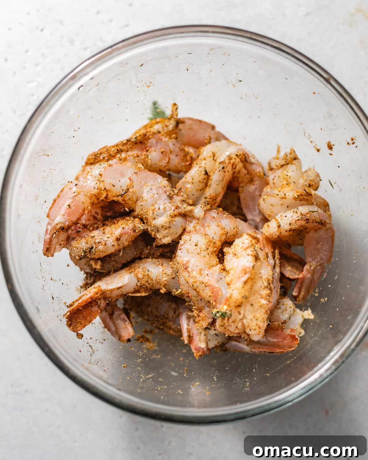 A bowl of fresh shrimp seasoned generously with a blend of spices, ready for stuffing and baking.