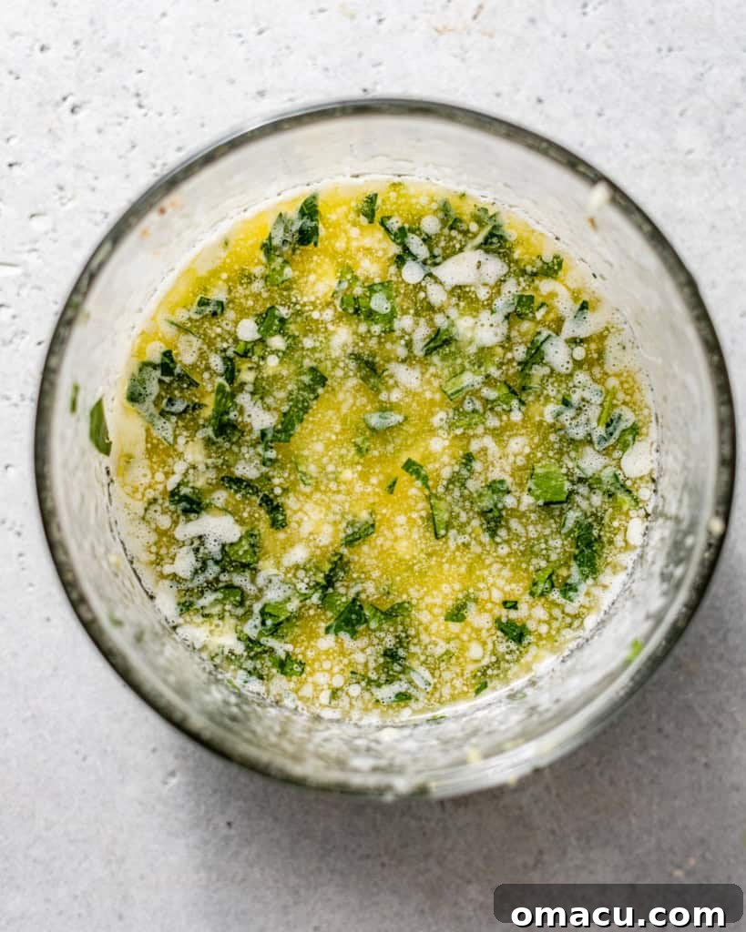 A small bowl containing a golden, aromatic garlic butter sauce, ready to be brushed over the stuffed shrimp.