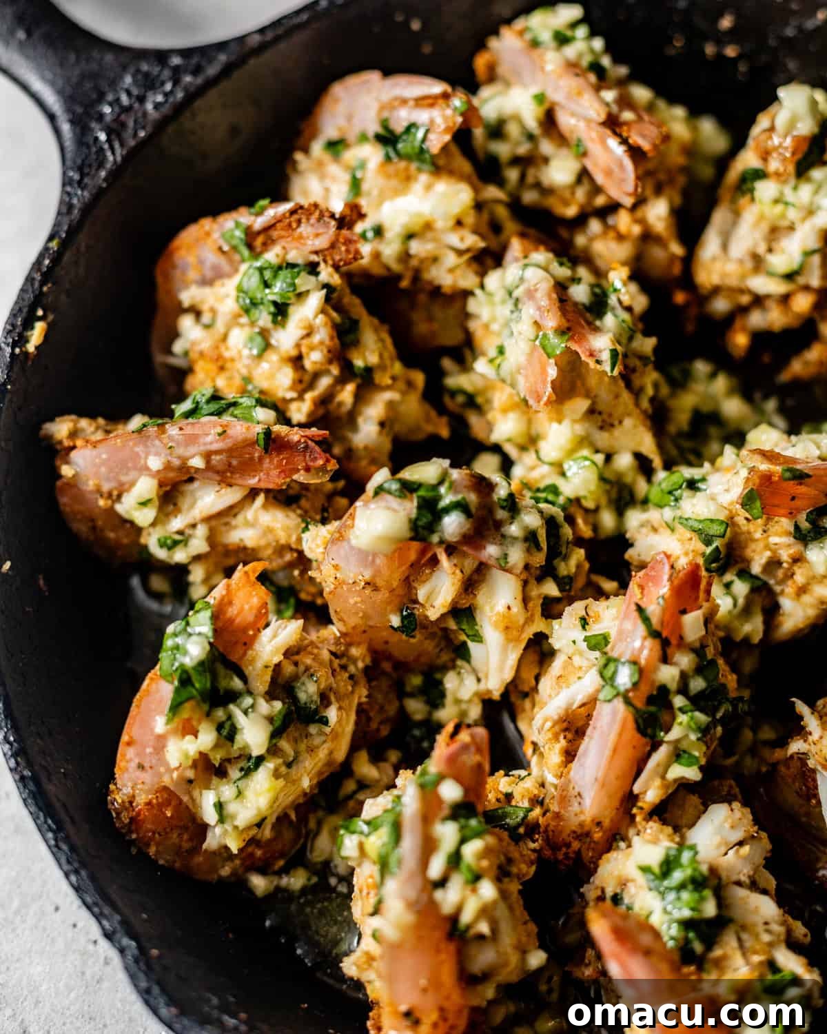 A cast iron skillet filled with crab stuffed shrimp, generously coated in a shimmering garlic butter sauce, ready for the oven.