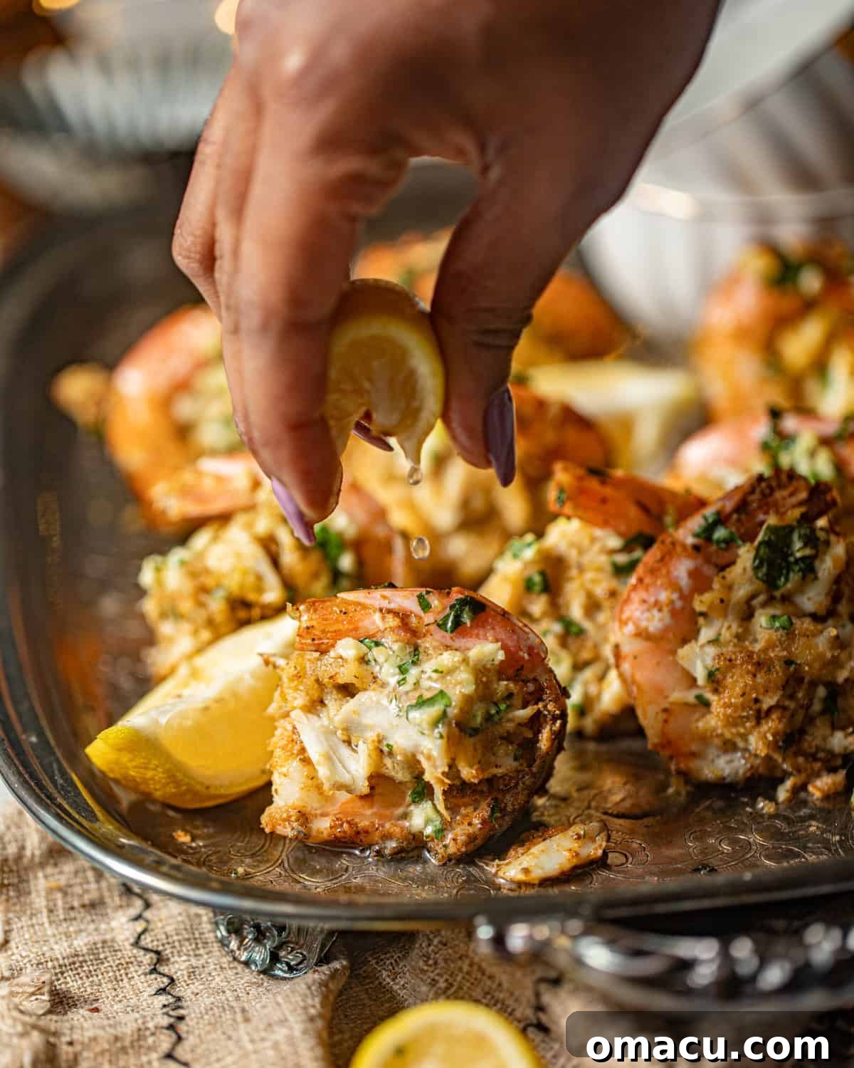 A hand expertly squeezing fresh lemon juice over the cooked crab stuffed shrimp, adding a final touch of brightness.