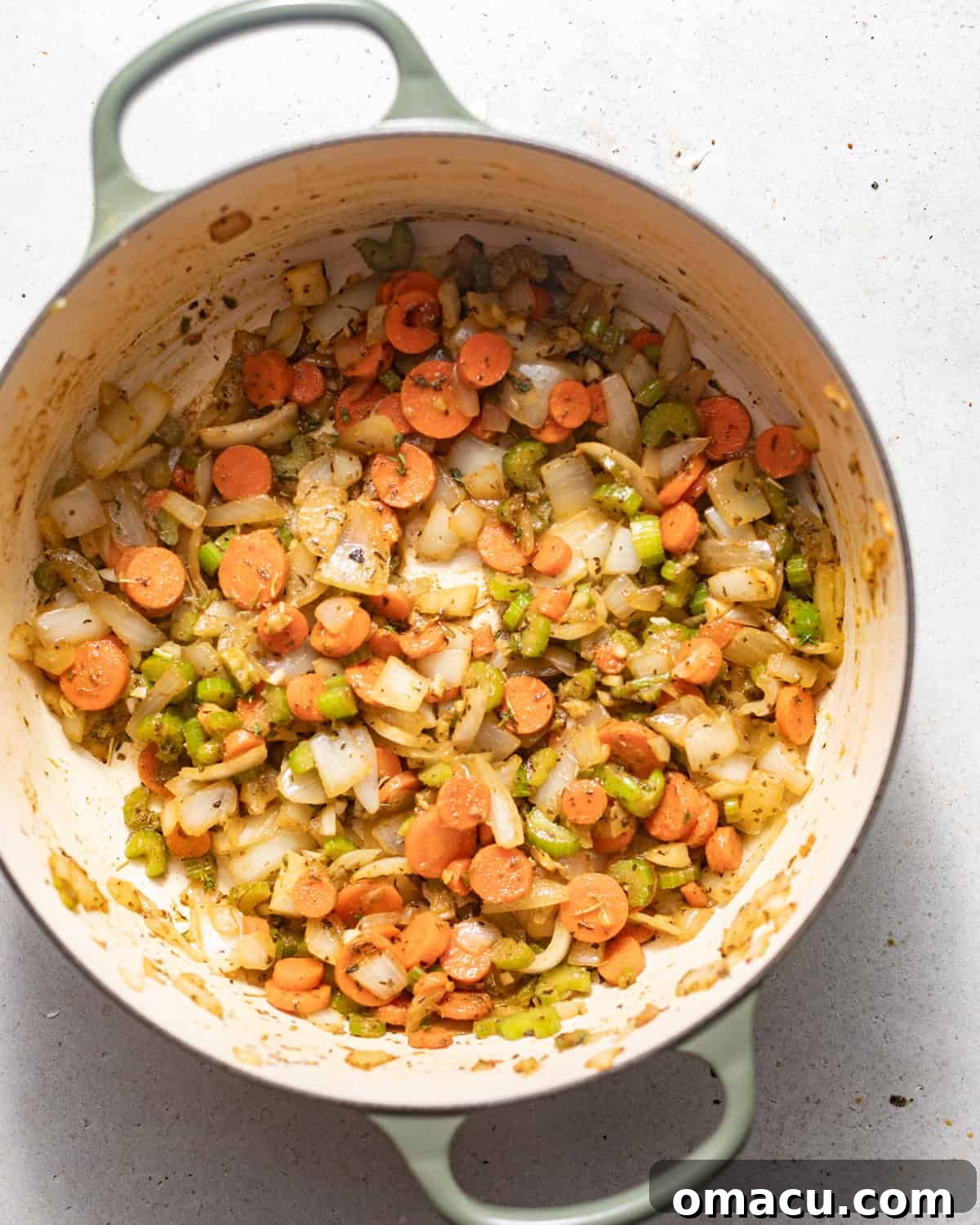 Diced onions, celery, carrots, and fresh garlic sautéing with aromatic seasonings in a large pot, filling the kitchen with fragrant smells.