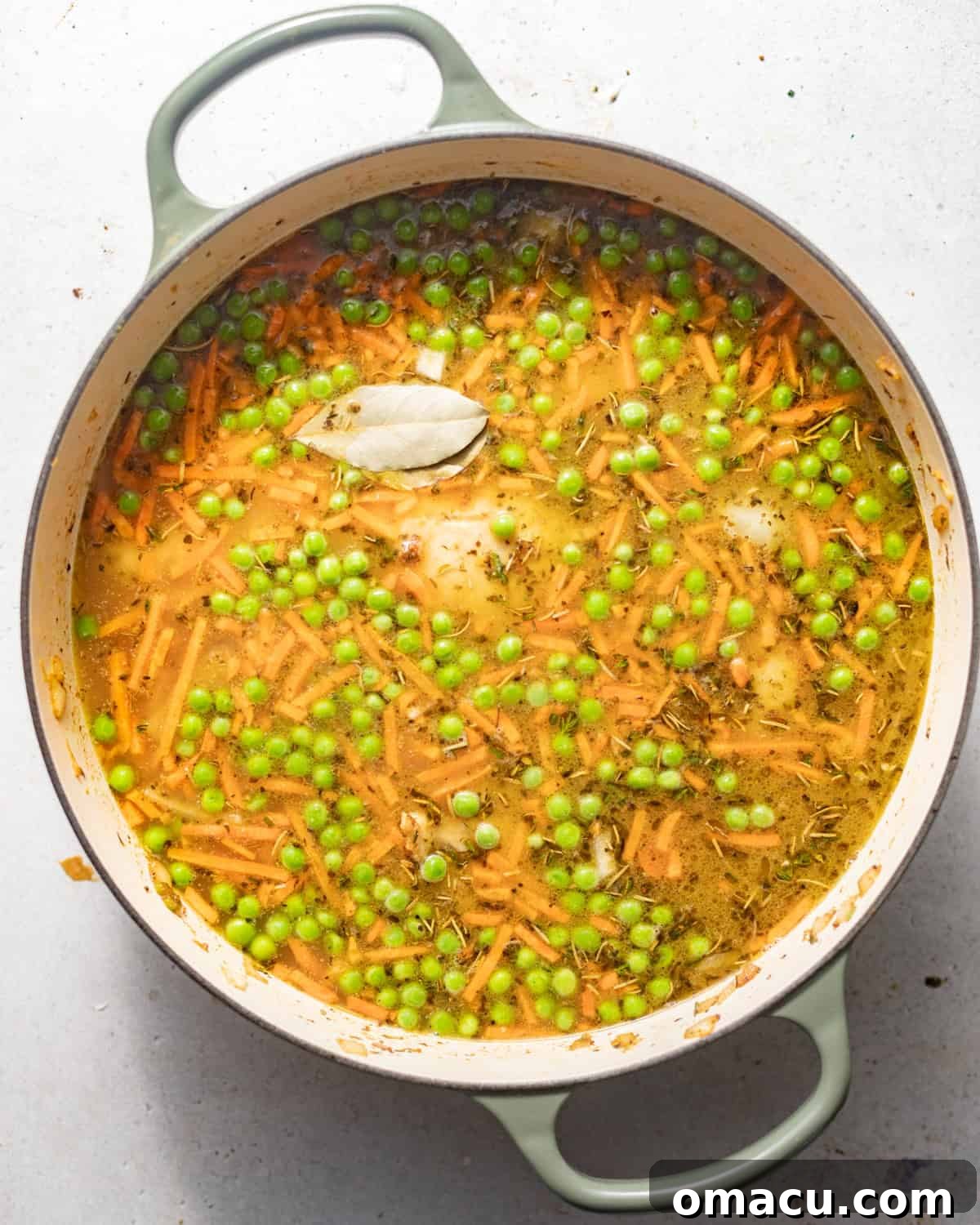 Chicken broth poured into a pot with sautéed vegetables, seared chicken thighs, and herbs, simmering gently.