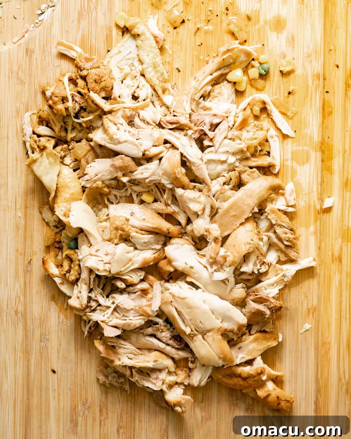 Shredded cooked chicken on a wooden cutting board, ready to be added back to the soup.