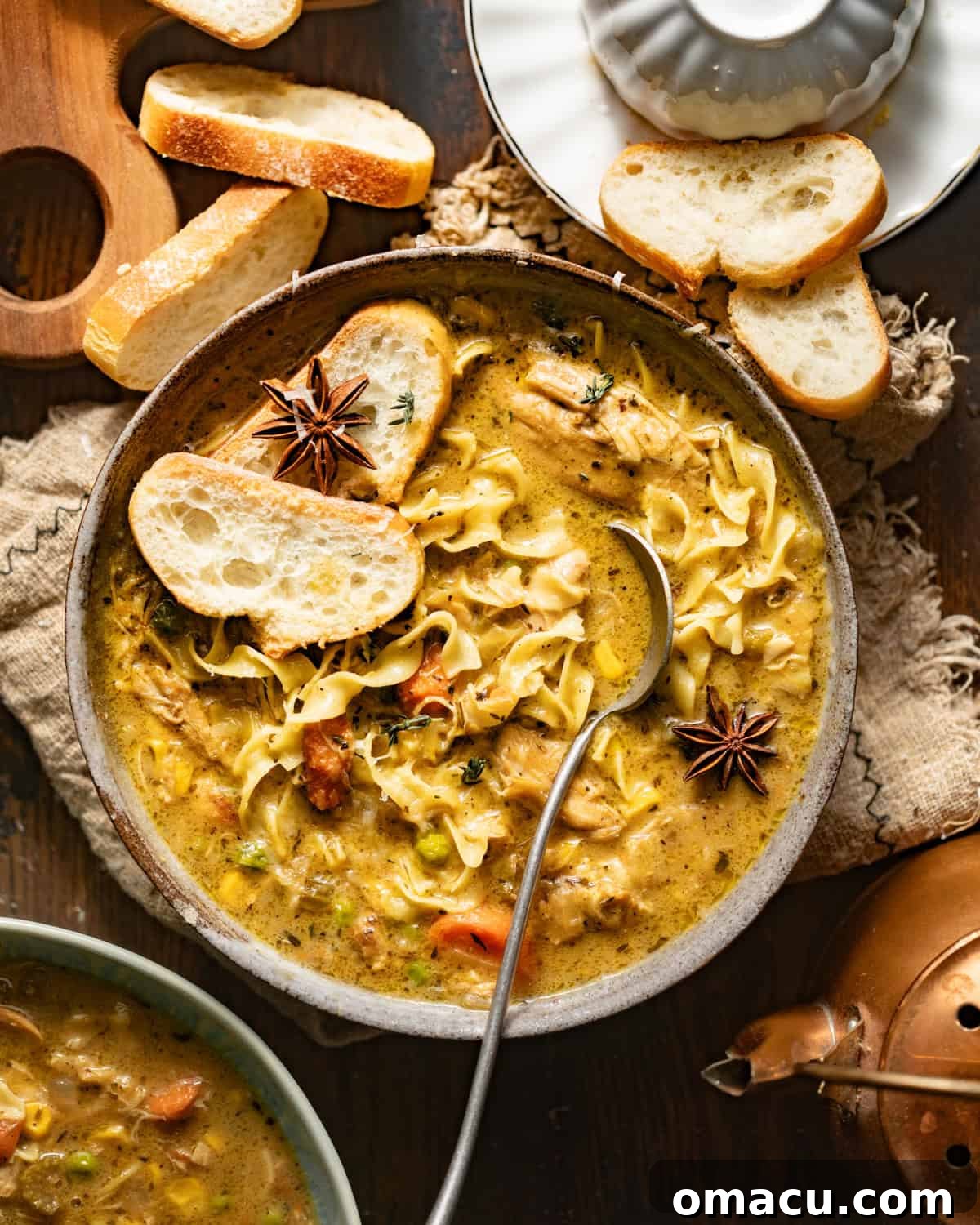 A large pot of creamy chicken noodle soup, garnished with star anise and fresh herbs, ready to be served with crusty bread.