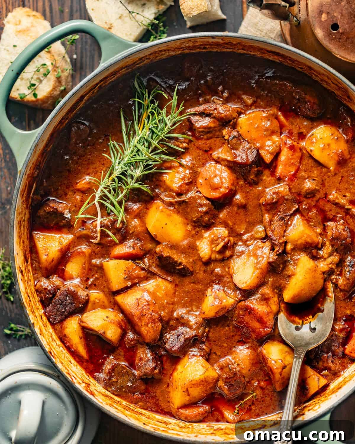 A large pot of stovetop beef stew, generously topped with fresh rosemary and thyme sprigs, ready to be served.