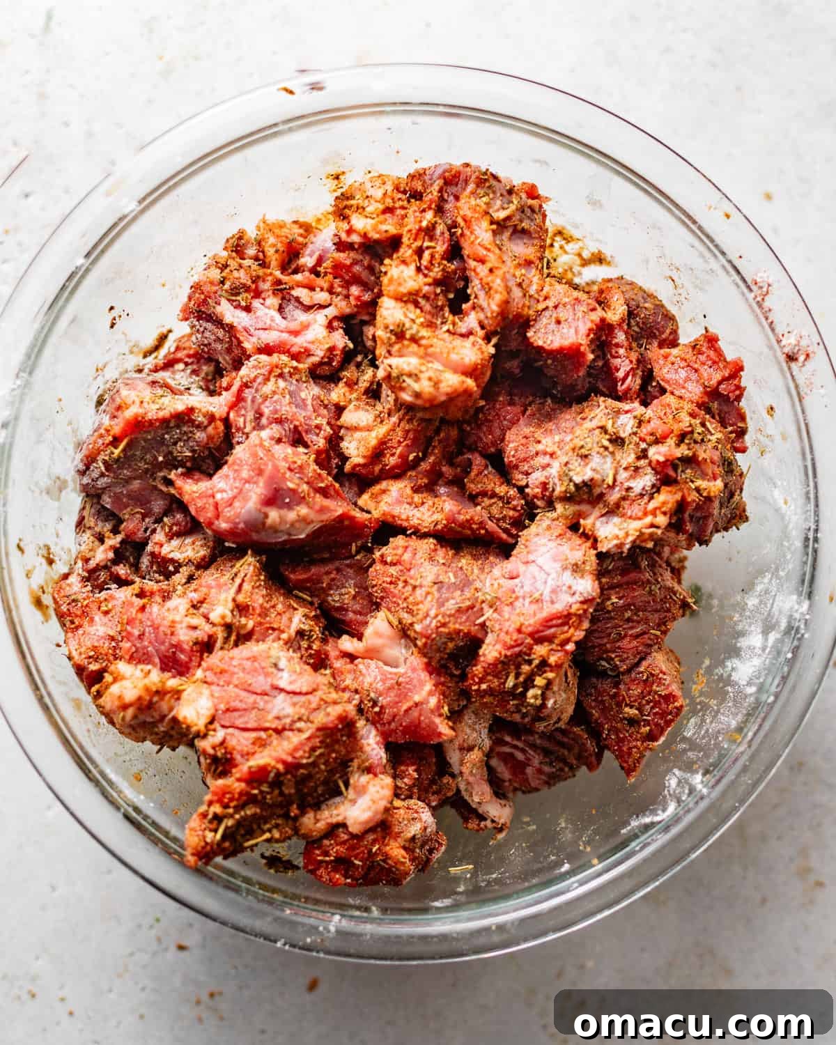 Chuck roast cut into uniform bite-sized chunks and thoroughly coated with seasonings and flour on a preparation surface.