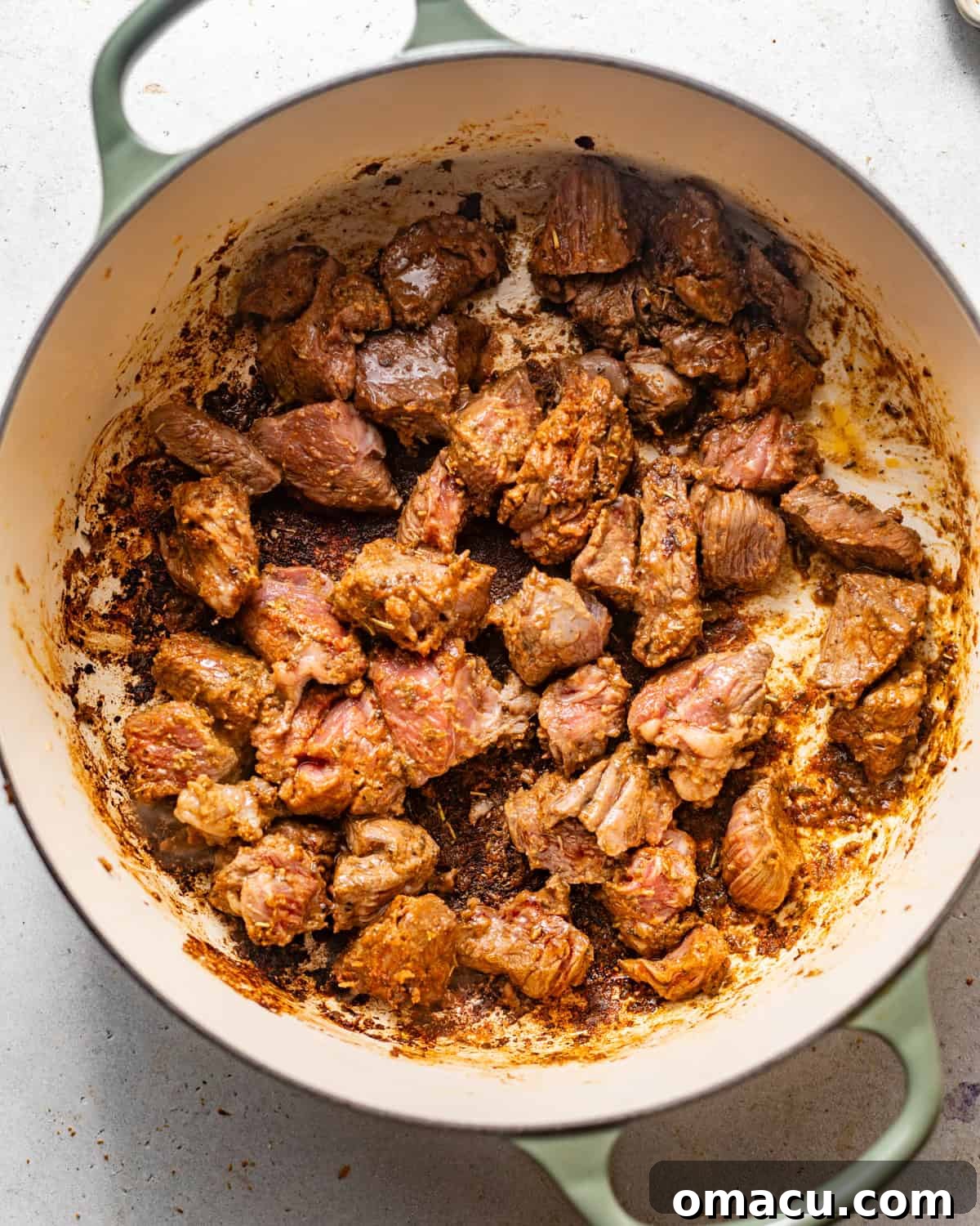 Perfectly seared, golden-brown beef chunks cooking in a large Dutch oven over medium-high heat.