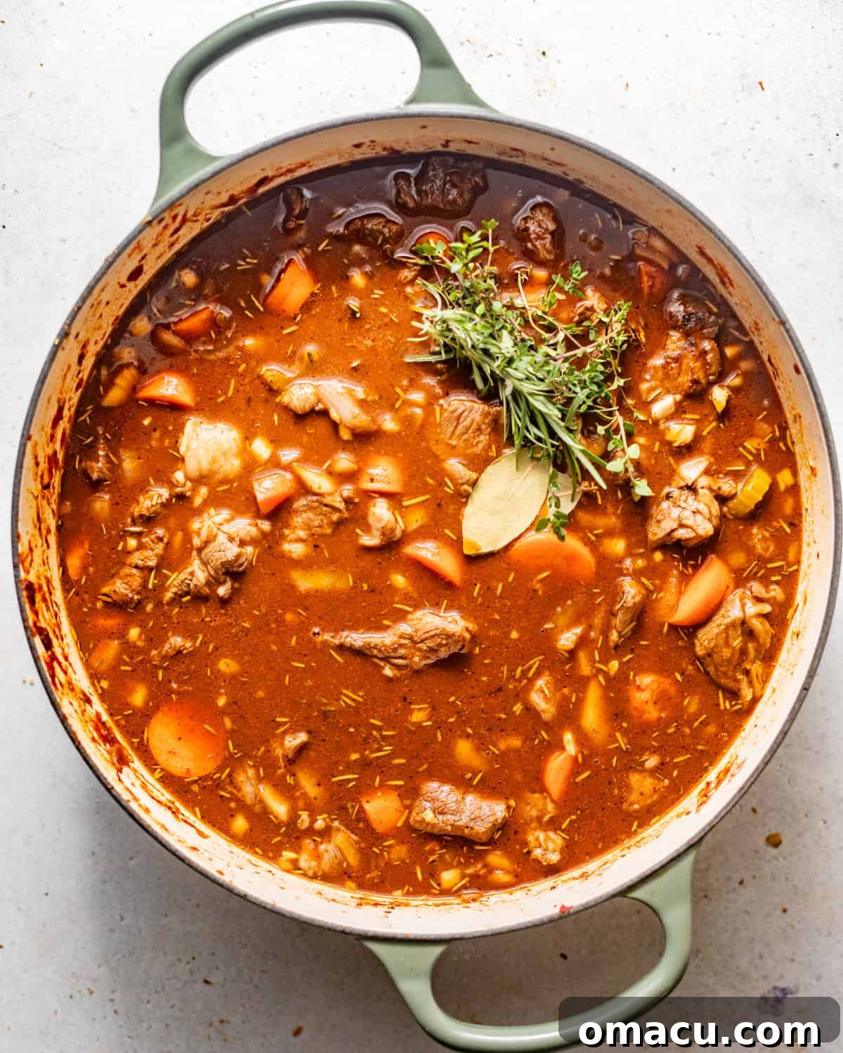 A large pot of hearty beef stew simmering gently on a stovetop, with a rich, thick broth and visible chunks of beef and vegetables.